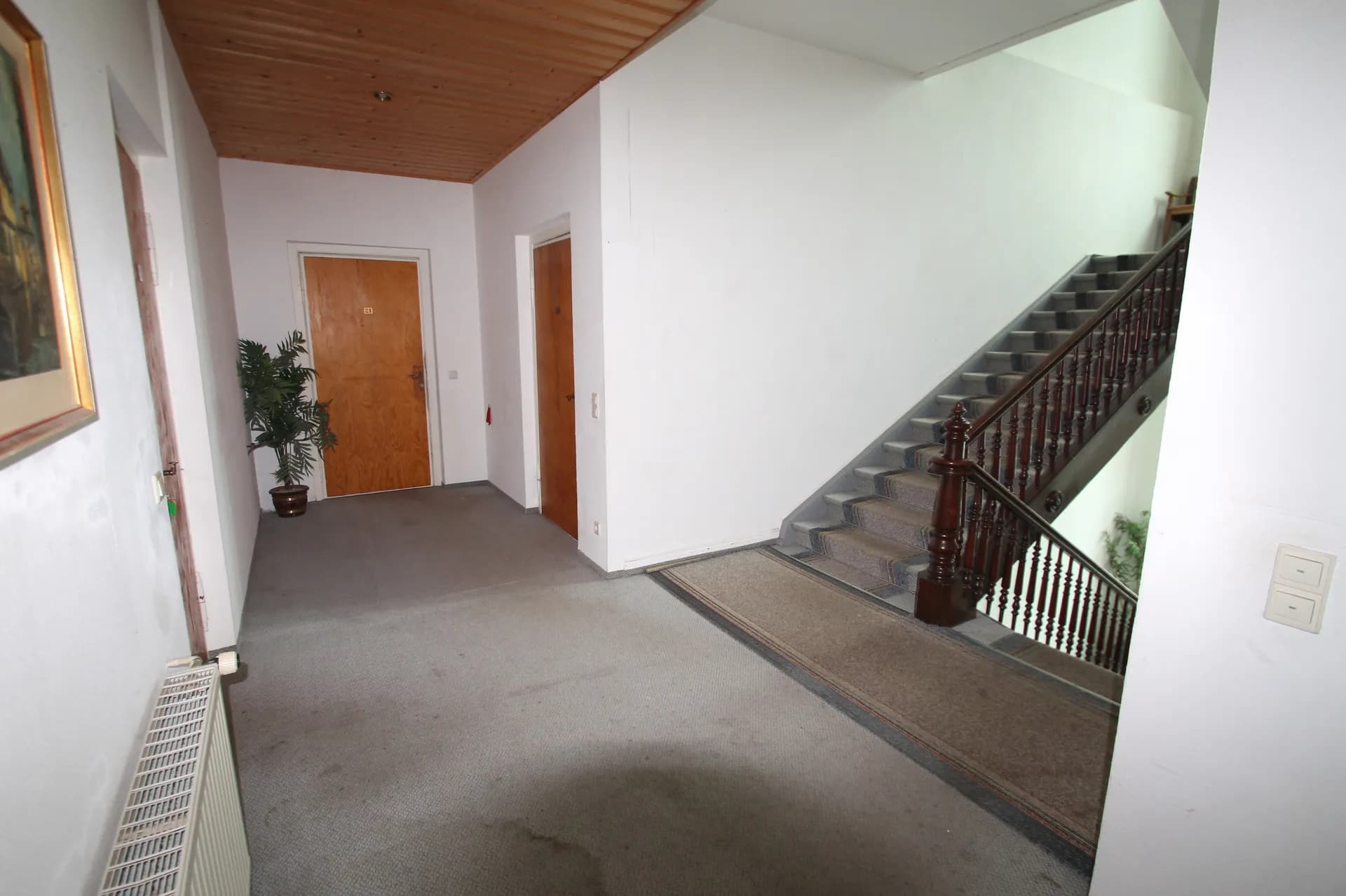 Großzügiger Treppenabsatz und Etagenflur des Hotels mit Teppichboden, Holzpaneeldecke, historischer Holztreppe mit gedrechselten Balustern und Zimmertüren.