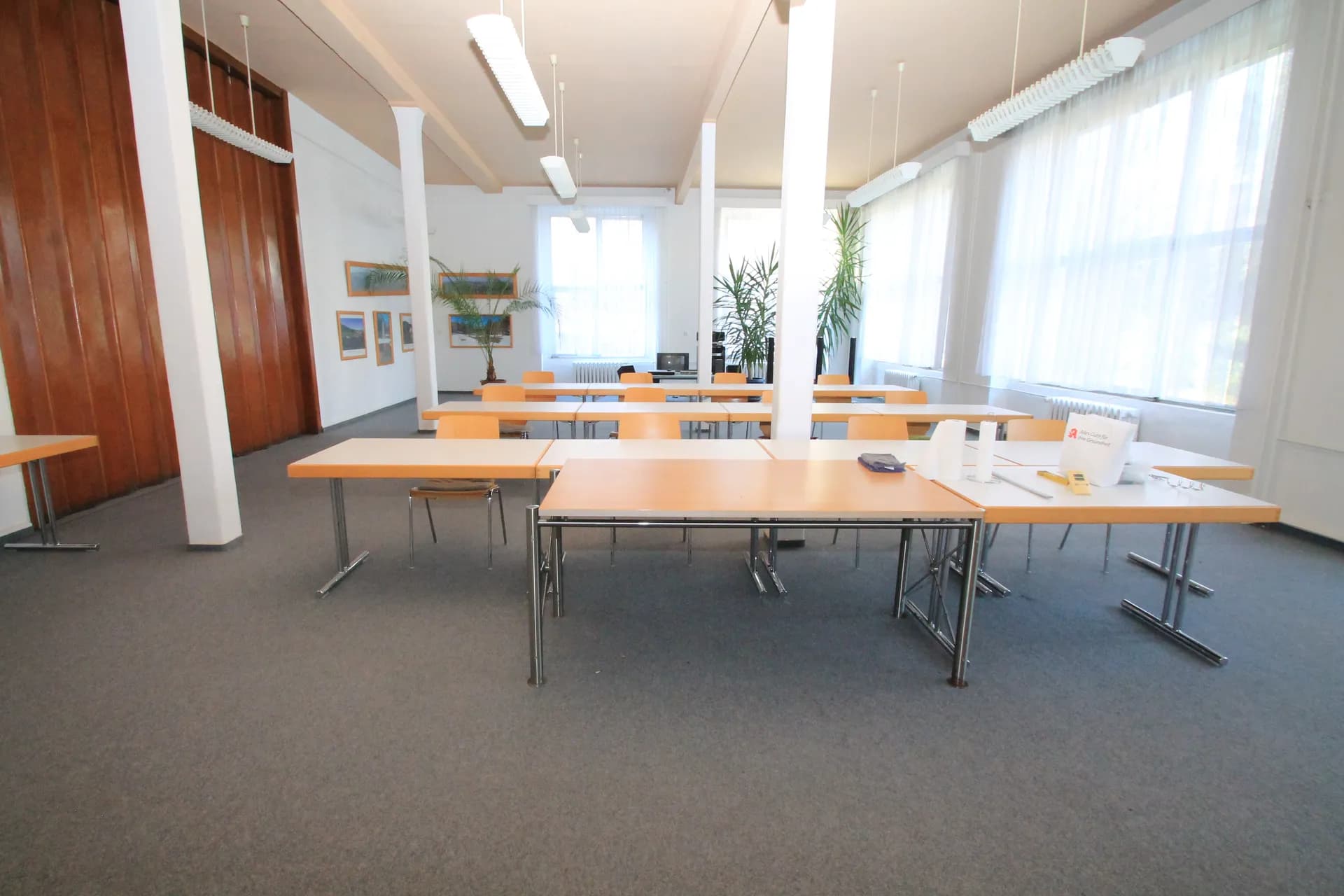 Lichtdurchfluteter Seminar- oder Schulungsraum mit großen Fensterfronten, Säulenstruktur, flexiblen Tischen samt Bestuhlung und Teppichboden.