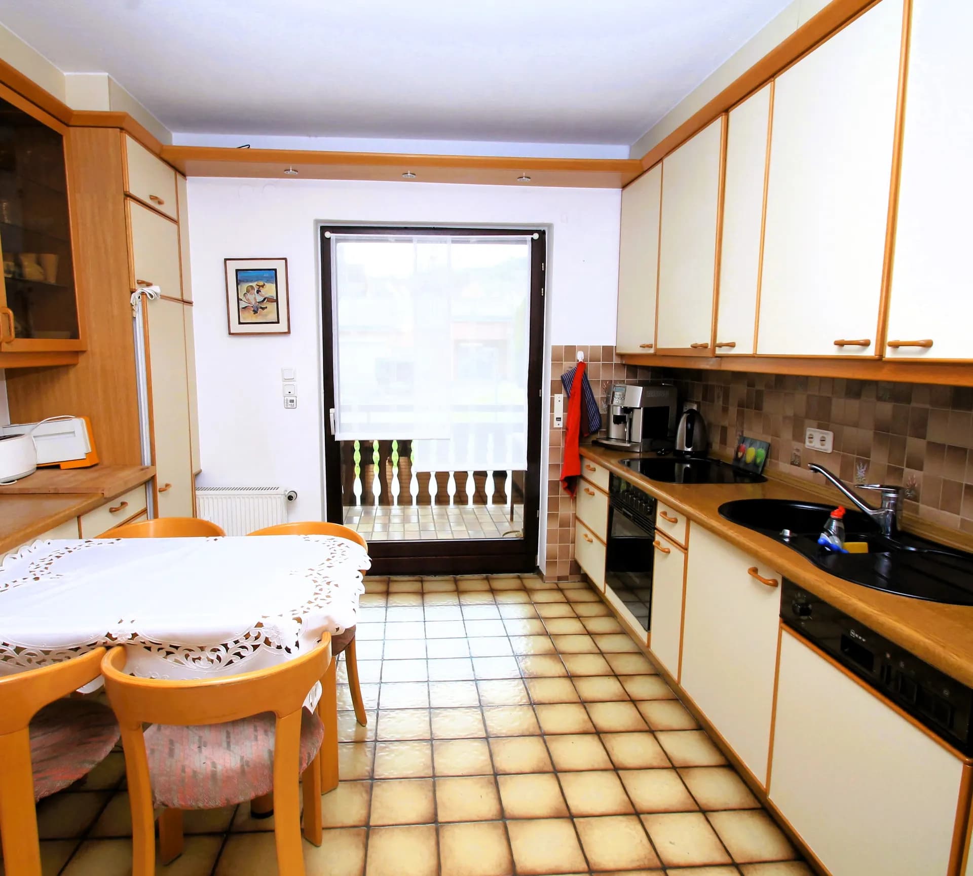 Geräumige Wohnküche mit heller Einbauzeile und Holzfurnier, Markengeräten, gemütlicher Essecke, Terrakottafliesen und direktem Zugang zum Balkon.