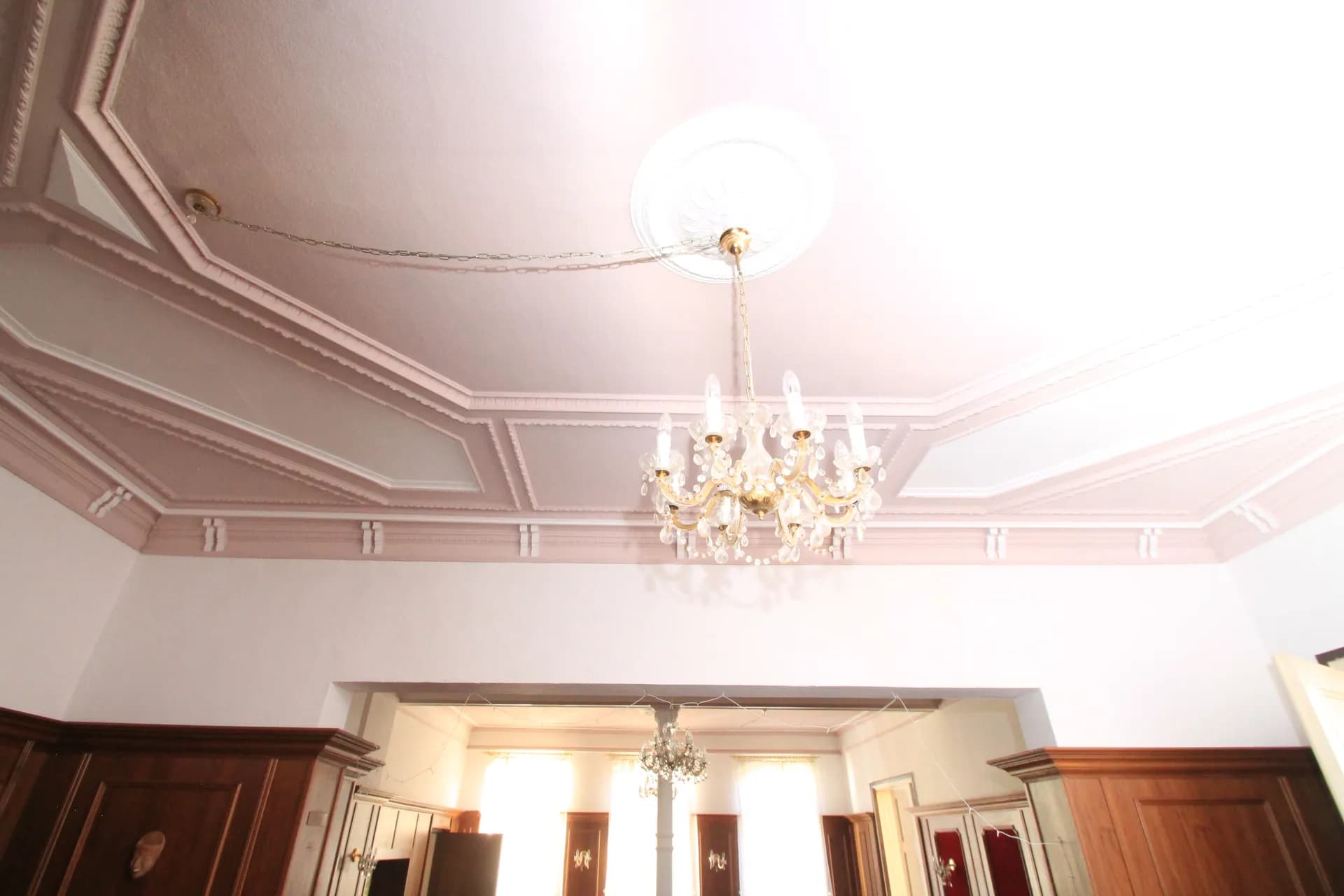 Detailansicht des Gaststätten-Innenbereichs mit aufwendiger Deckenstuckatur, Zierkassetten, elegantem Kristalllüster und massiver Holz-Wandvertäfelung.