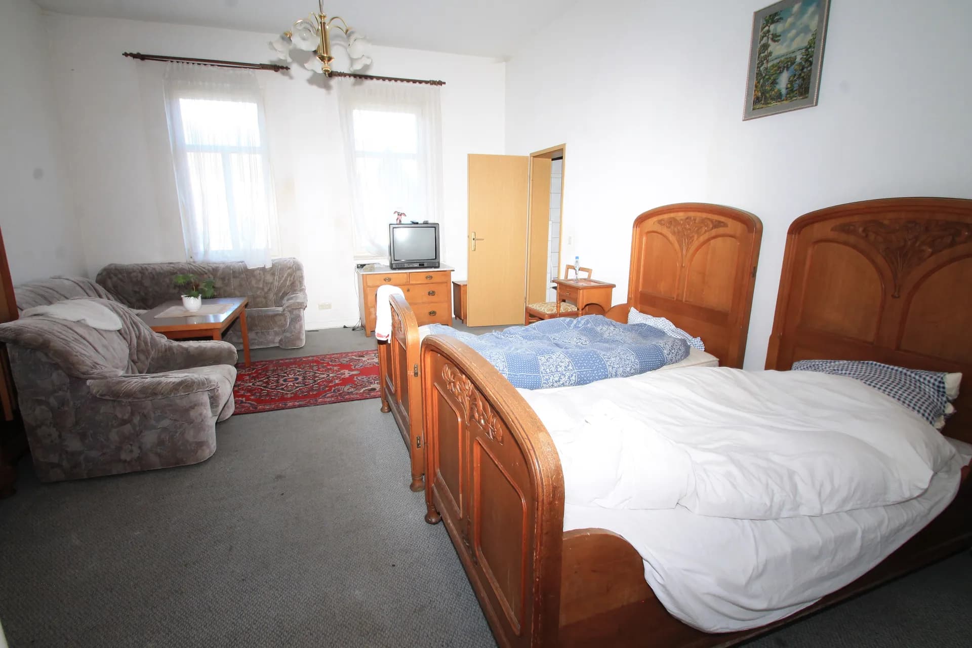 Geräumiges Hotelzimmer mit zwei klassischen Massivholz-Einzelbetten, TV-Kommode, gemütlicher Sitzecke samt Sessel, Sofa und Couchtisch sowie Orientteppich.