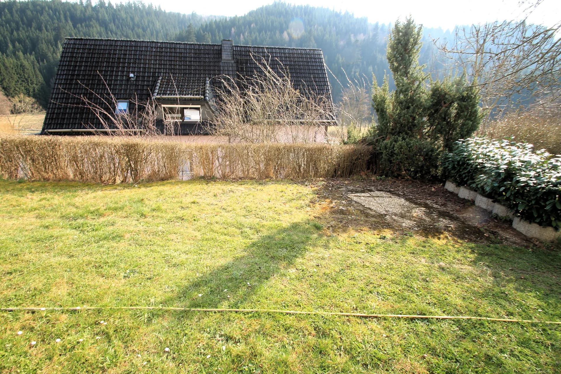 Idyllischer Gartenbereich mit Rasenfläche, Heckenabgrenzung und weitem Blick auf die bewaldeten Hänge.