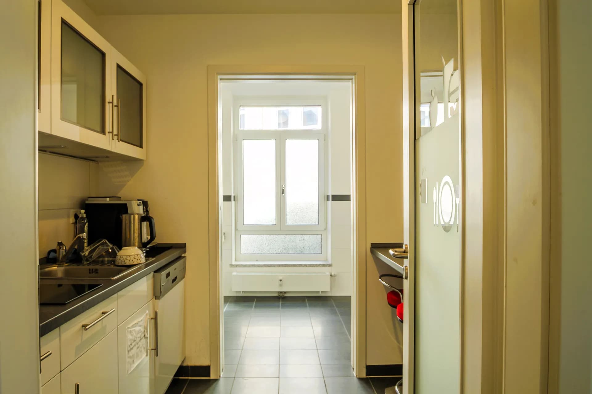 Moderne Teeküche der Büroeinheit in Hof mit Einbauzeile, Edelstahlspüle, Geschirrspüler, Kaffeemaschine und Fensterfront zum angrenzenden Raum.