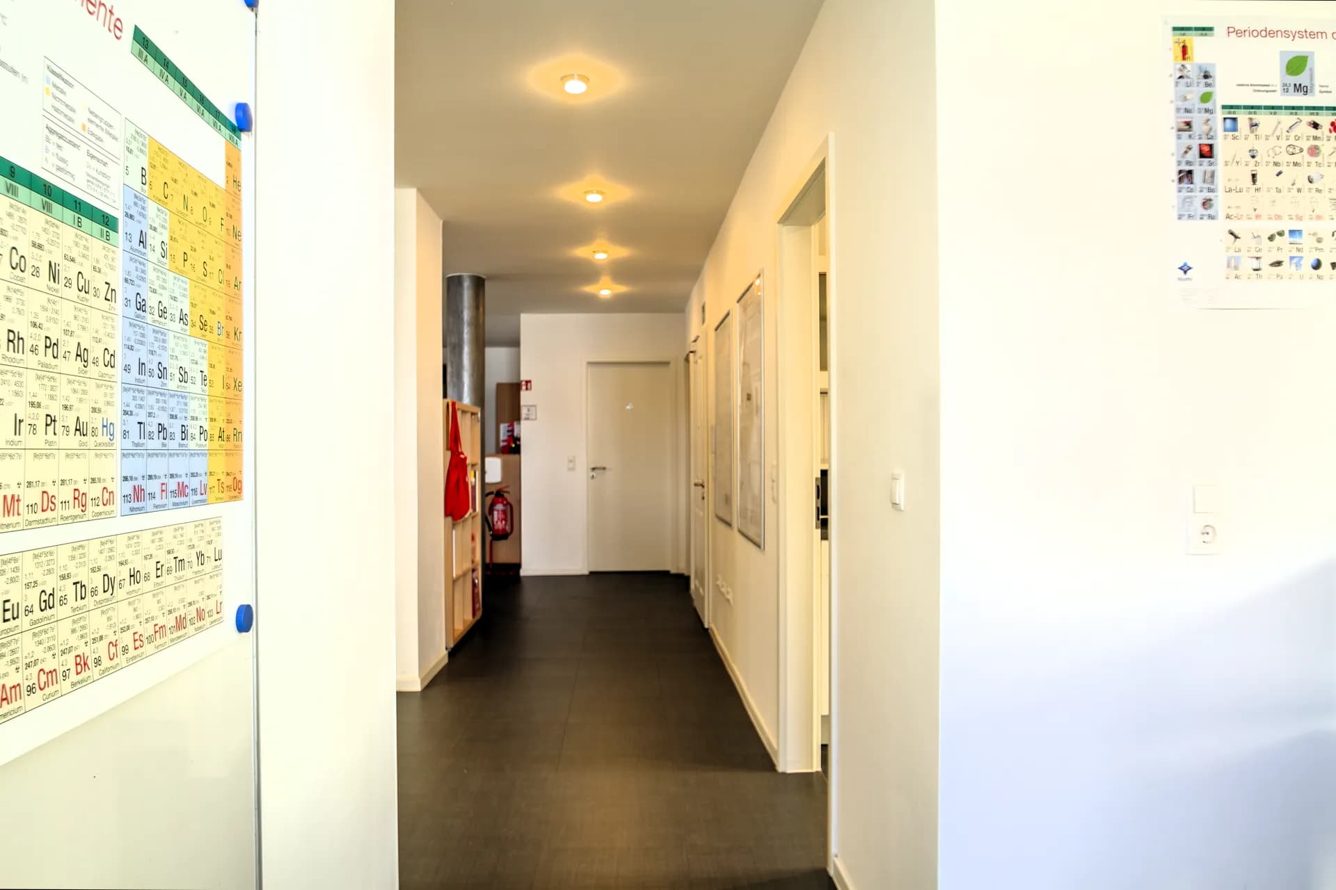 Zentraler Büroflur in Hof mit Deckenspots, dunklem Fliesenbelag, Informationstafeln an den Wänden und Zugängen zu den einzelnen Büroräumen.