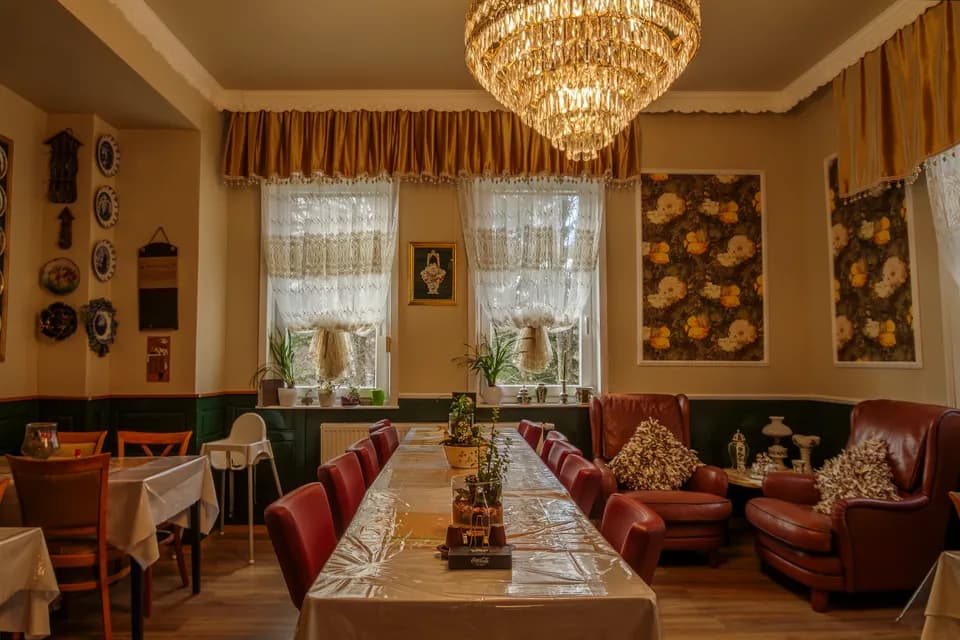 Gemütlicher Fest- und Speisesaal mit opulentem Kristallkronleuchter, langer festlicher Tafel mit roten Lederstühlen, Kamin-/Sitzecke mit Ohrensesseln und dekorativen Wandtellern.