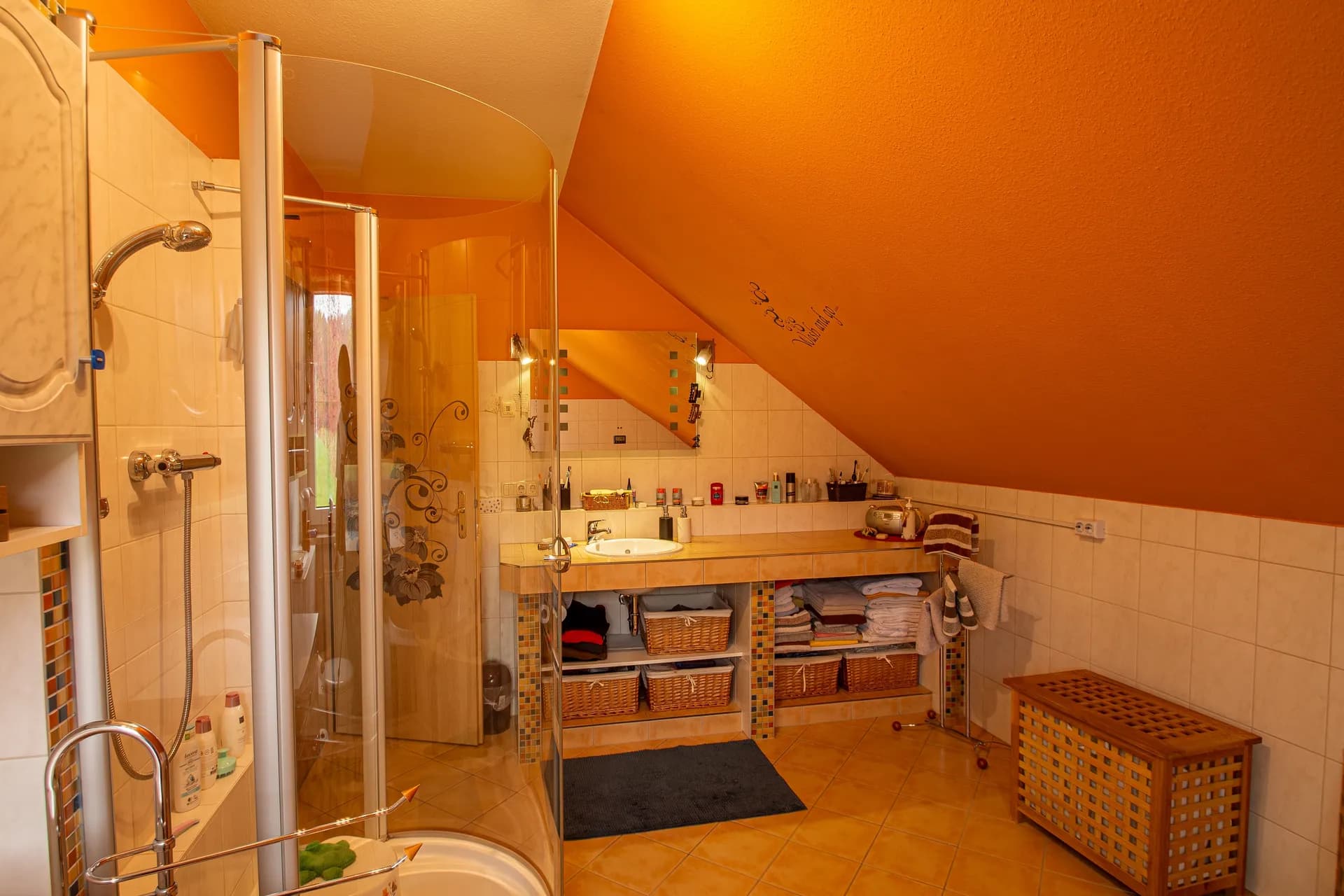 Badezimmerbereich mit moderner Glas-Duschkabine, gefliestem Waschtisch und offenem Stauraum.