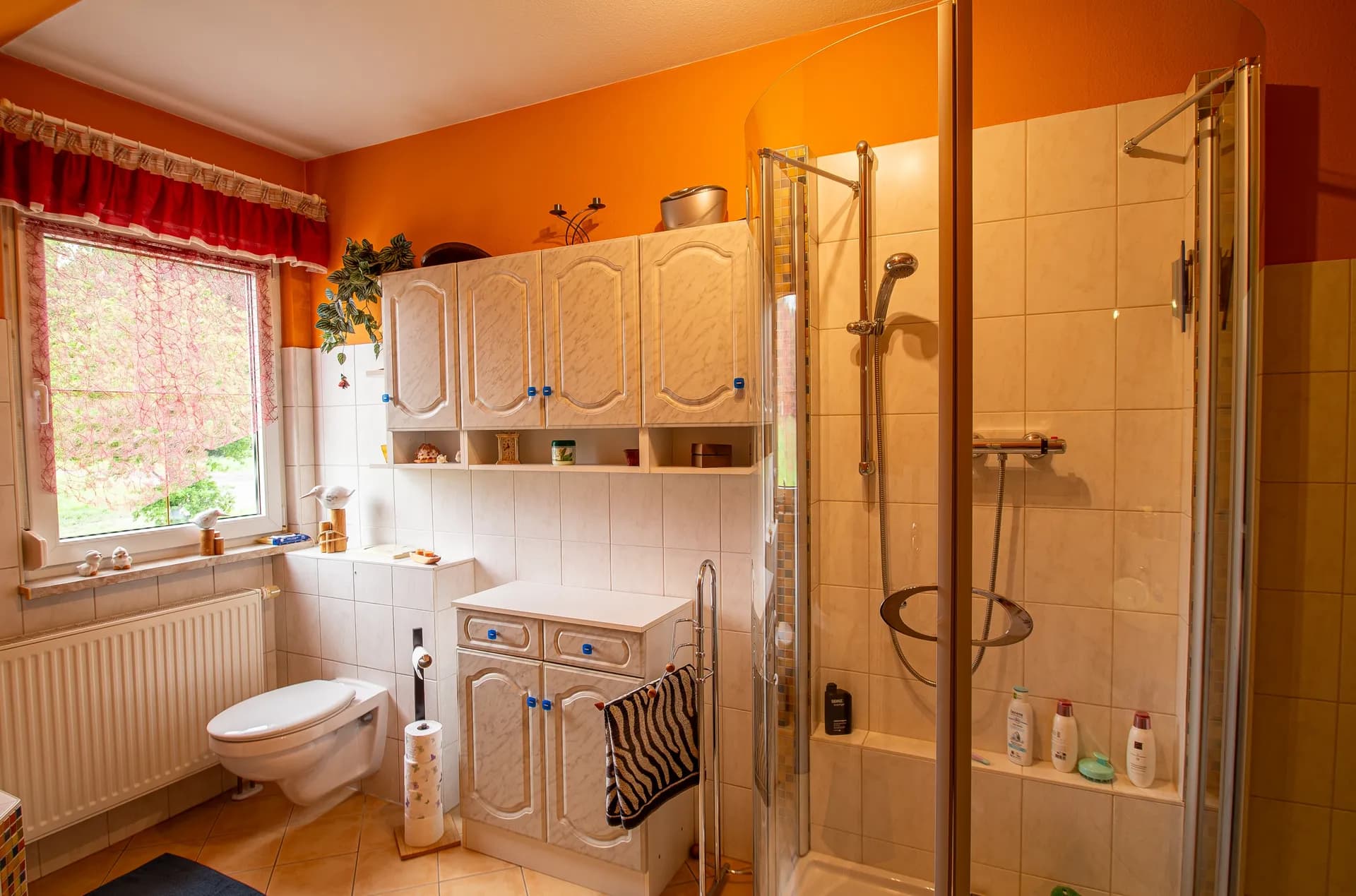 Helles Dachbad mit eingebauter Badewanne, Fliesenverkleidung, Fenster und weißen Hängeschränken.