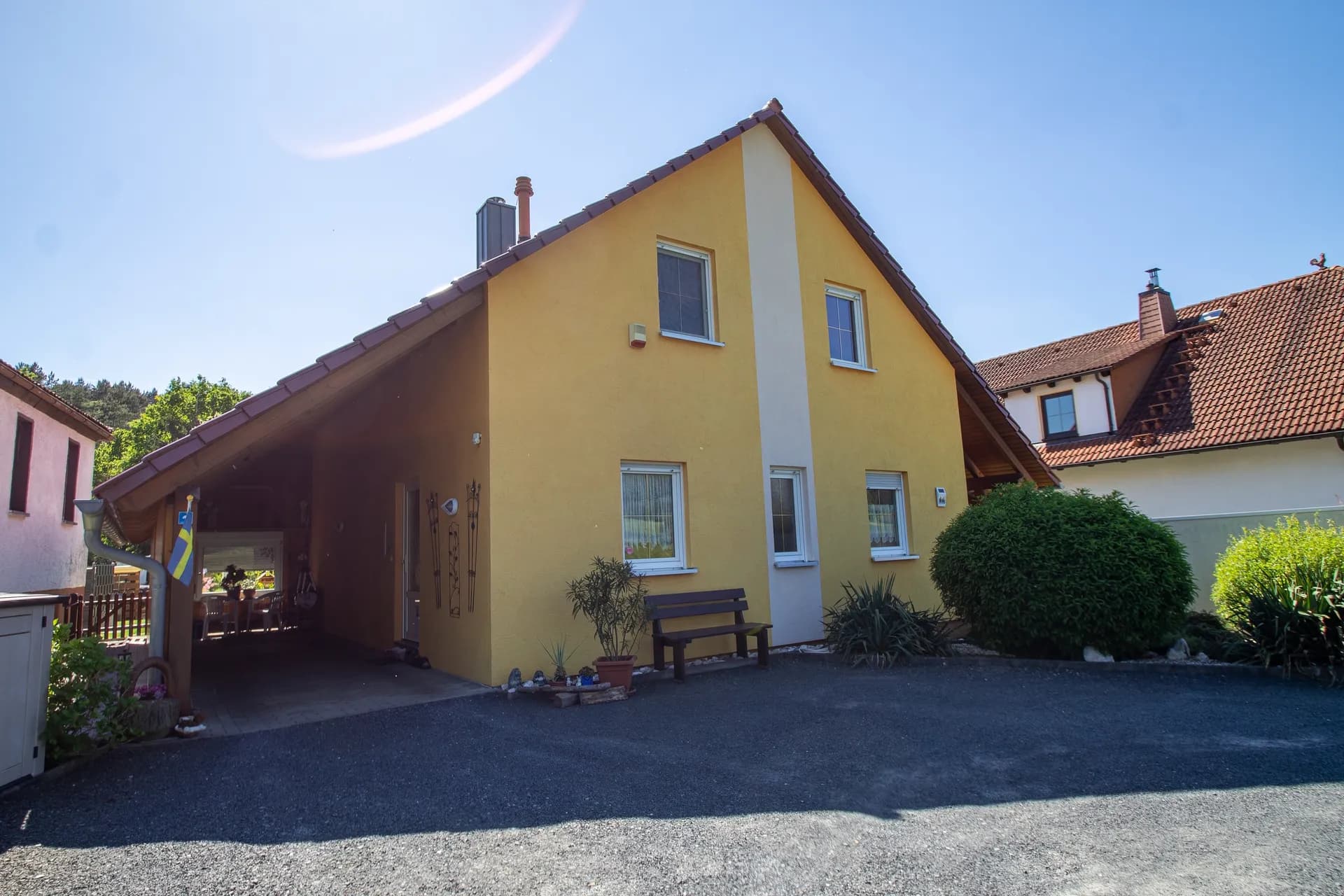 Straßenseitige Ansicht des gelben Einfamilienhauses mit Carport, separater Fertiggarage und gepflastertem Hof.