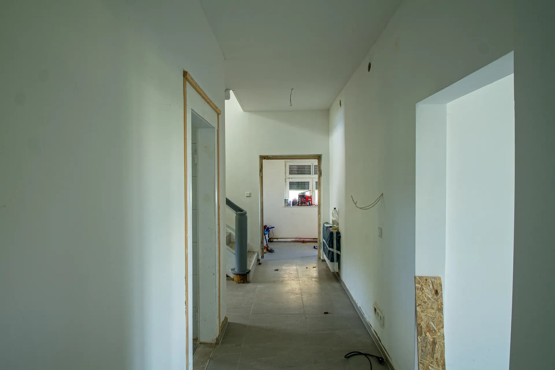 Breiter Hausflur im Erdgeschoss mit weißen Wänden, grau gefliestem Boden und Durchblick zum Treppenhaus.