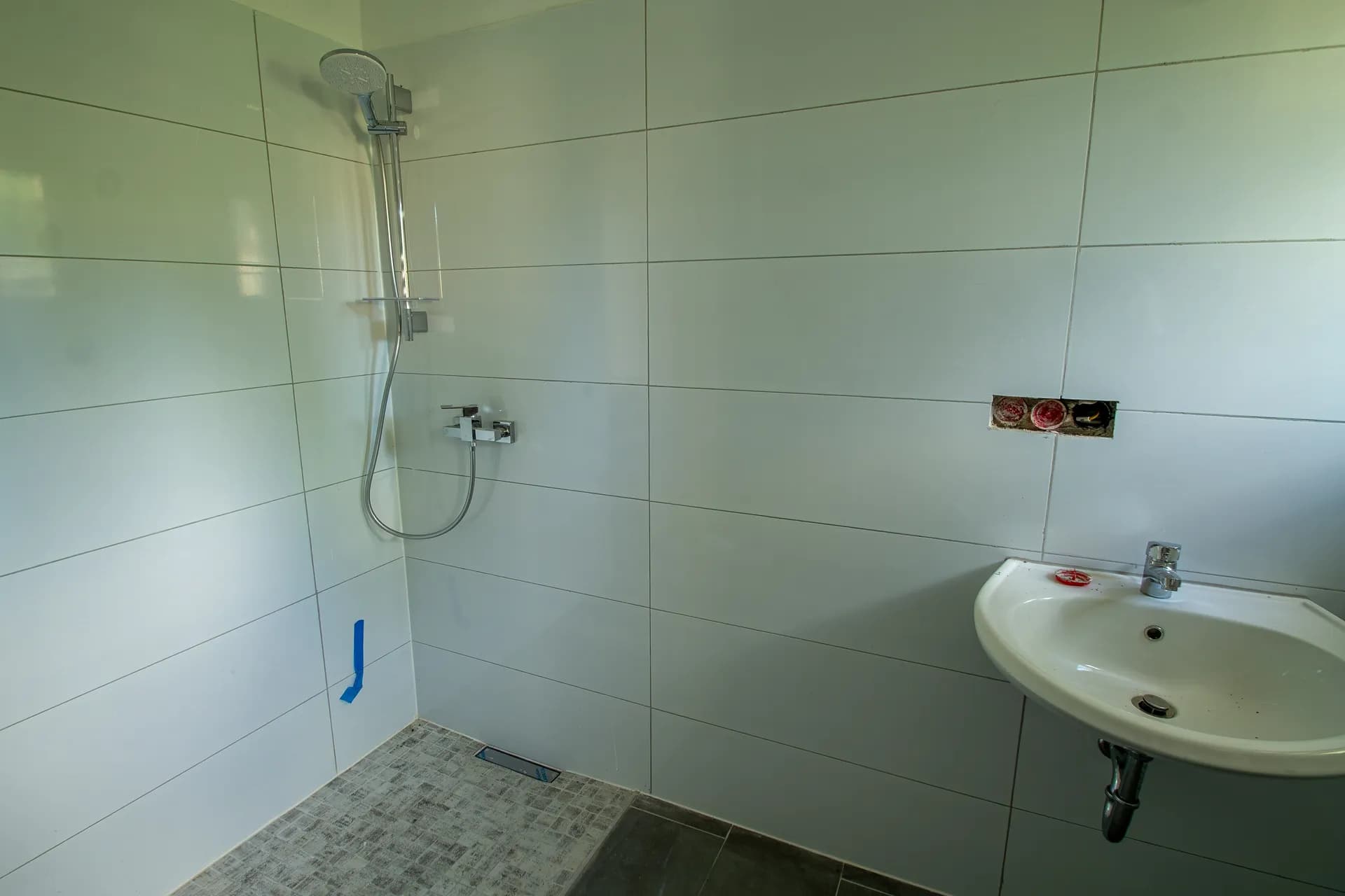 Modernes Badezimmer mit großformatigen weißen Fliesen, bodengleicher Dusche und wandhängendem Waschbecken.