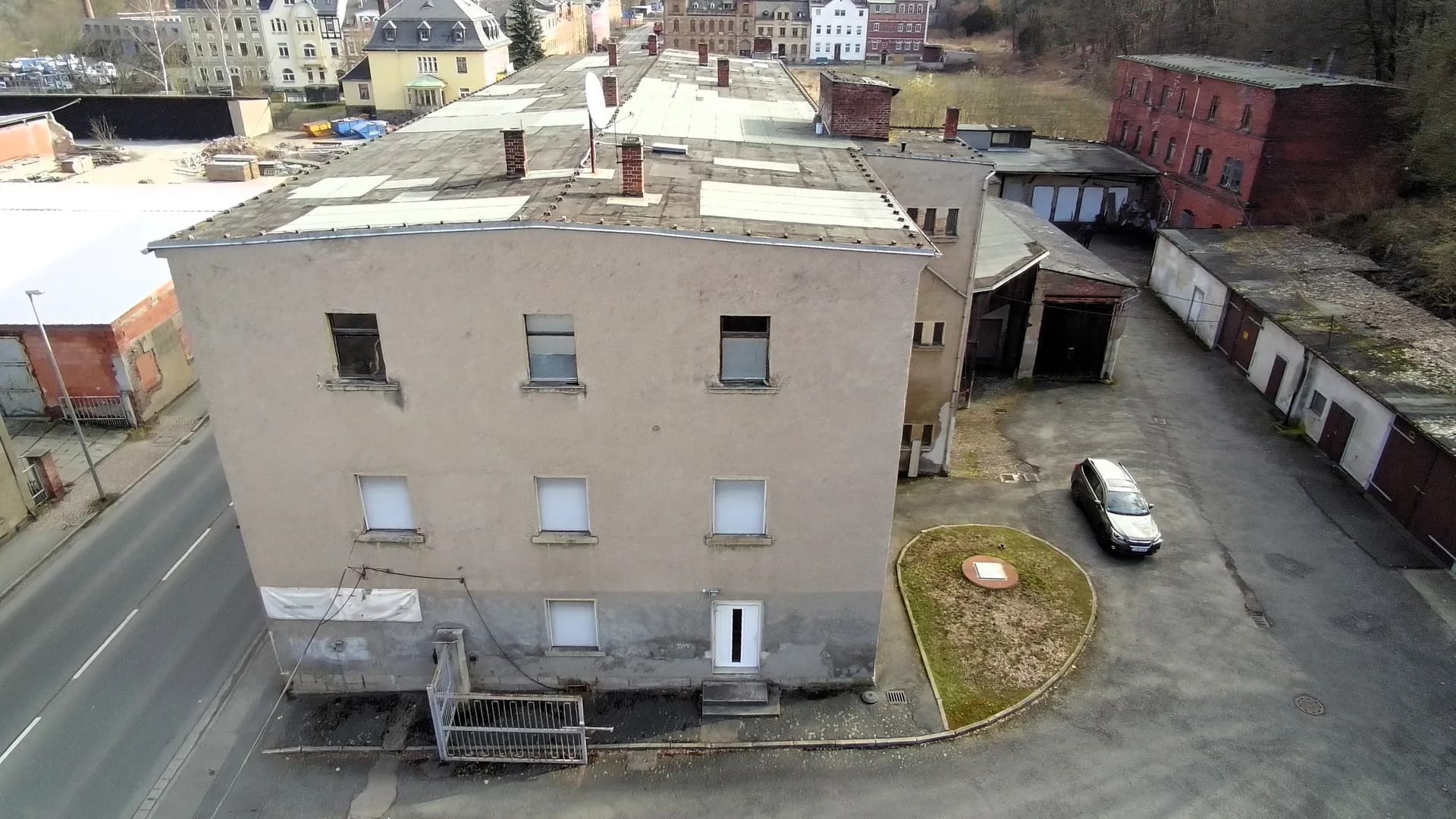 Giebelseite des mehrgeschossigen Gebäudekomplexes mit regelmäßig angeordneten Fenstern, Erdgeschosszugang, asphaltiertem Hofbereich und angrenzender Garagenanlage.