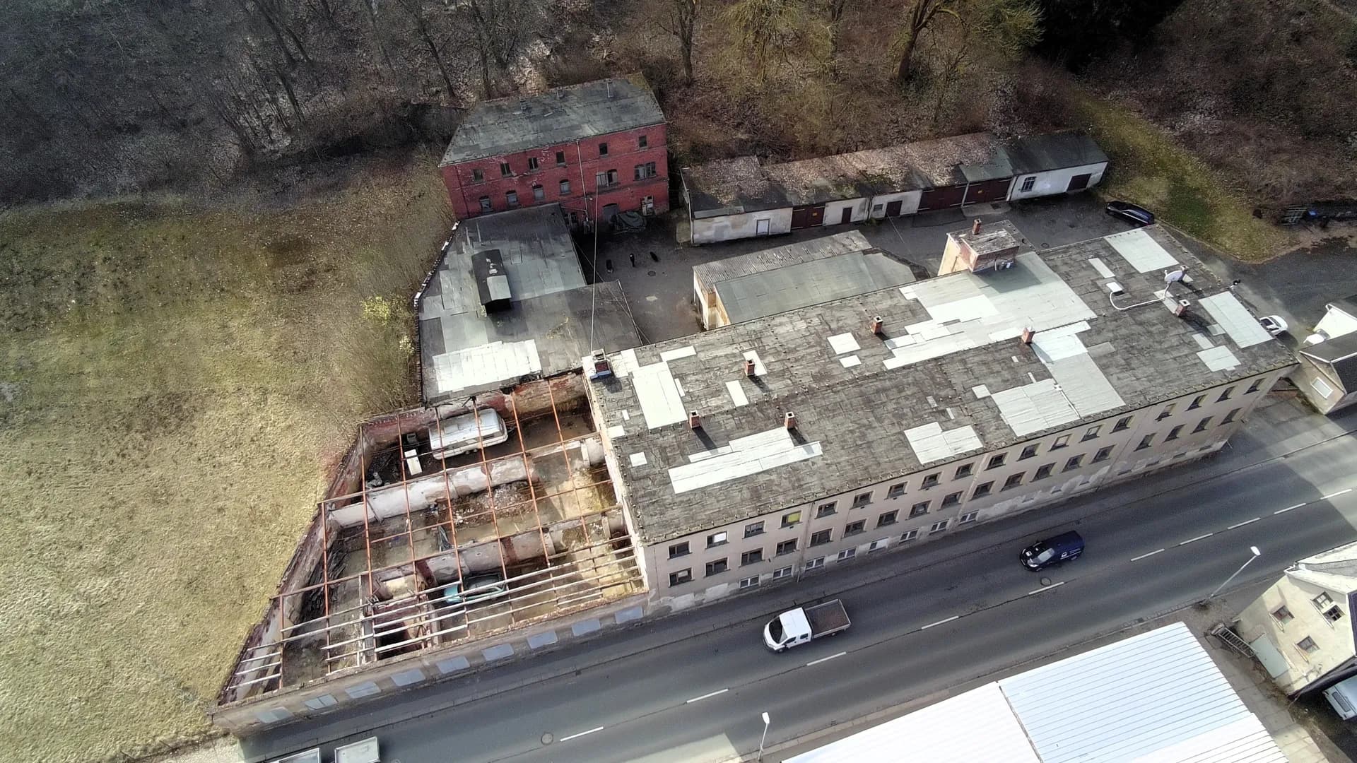 Vogelperspektive des Industrie- und Gewerbekomplexes: langgestreckter Haupttrakt entlang der Straße, teilentkernter Gebäudeteil mit offenem Dachtragwerk, Innenhof samt Garagenzeilen und rückwärtiges Backsteingebäude.
