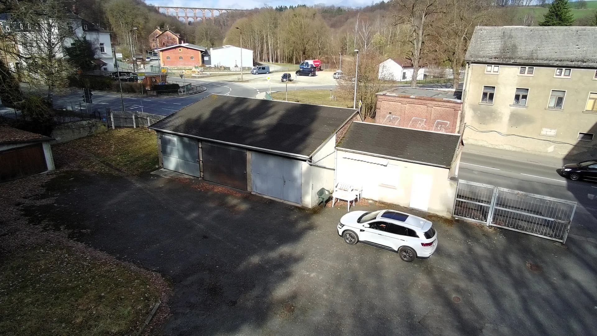 Asphaltierter Hofbereich des Gewerbeareals mit separater Garagenanlage, Nebengebäude, Gitter-Zufahrtstor und historischem Eisenbahnviadukt im Hintergrund.