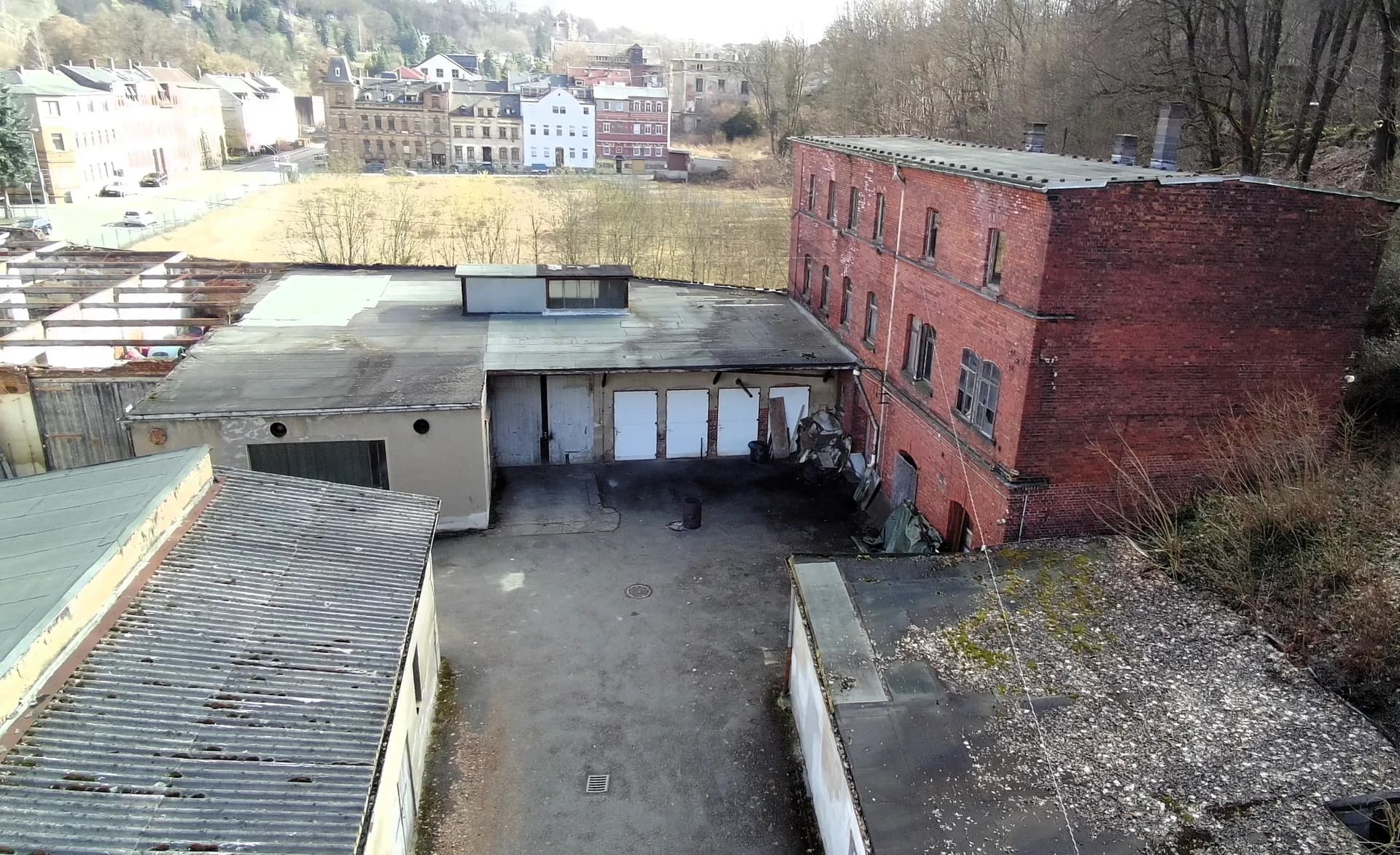 Rückwärtiger Werkhof mit Laderampe, Werkstatttoren, Flachdachanbauten und historischem, mehrgeschossigen Industrie-Backsteinbau.