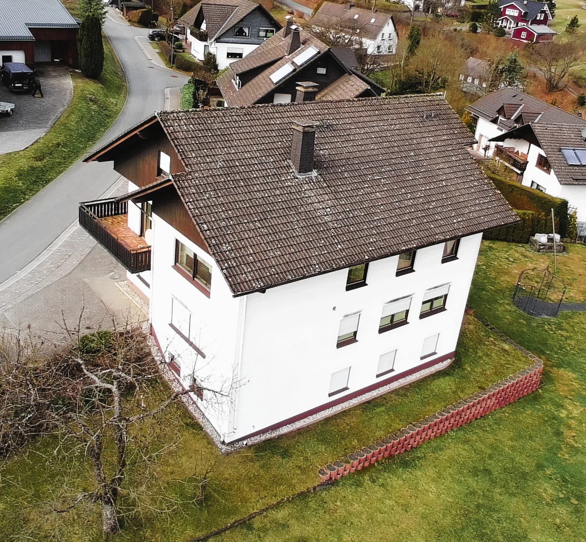Drohnenaufnahme der Rückfassade und des Satteldachs des Wohnhauses: terrassierte Rasenfläche mit Pflanzsteinen, Fensterreihen über drei Etagen und Blick auf die umliegende Ortschaft.