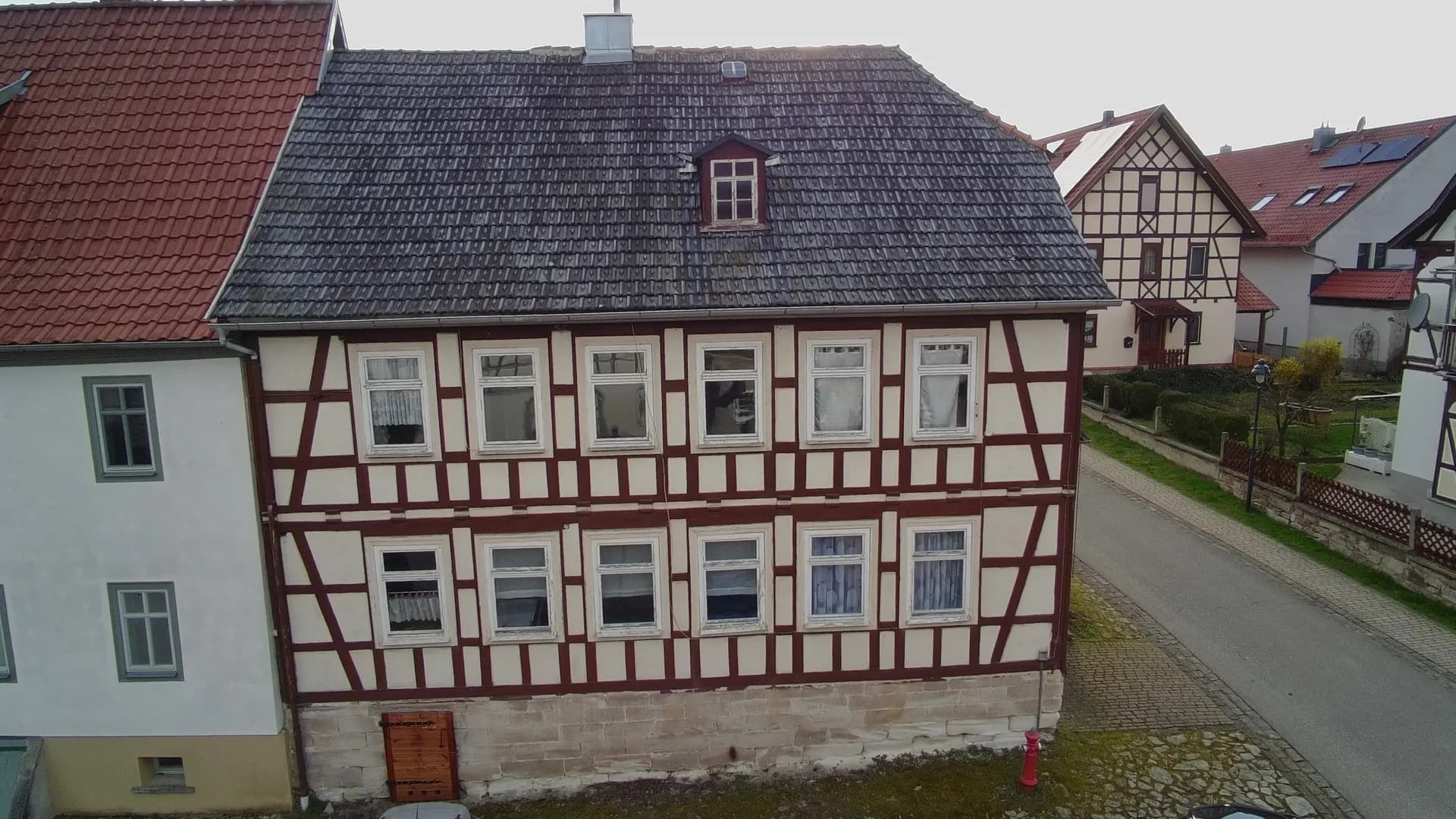 Fassadenansicht des traditionellen Fachwerkhauses mit Sandsteinsockel, symmetrischer Fensteranordnung, Ziegeldach und kleiner Dachgaube.