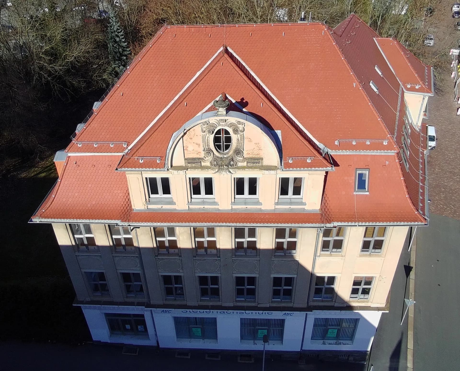 Luftaufnahme der Frontfassade mit Fokus auf den reich verzierten Jugendstil-/Neobarockgiebel, das ovale Ochsenauge-Fenster und die symmetrische Fenstergliederung.