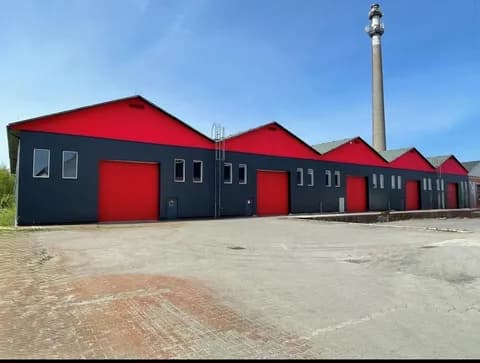 Moderne Gewerbe- und Lagerhalle mit markanter rot-schwarzer Fassade, mehreren Sektionaltoren, Antennenmast und großzügiger gepflasterter Hoffläche zur Anfahrt.