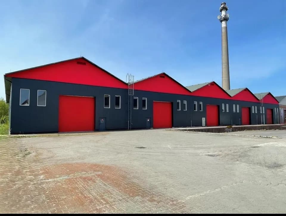 Moderne Gewerbe- und Lagerhalle mit markanter rot-schwarzer Fassade, mehreren Sektionaltoren, Antennenmast und großzügiger gepflasterter Hoffläche zur Anfahrt.