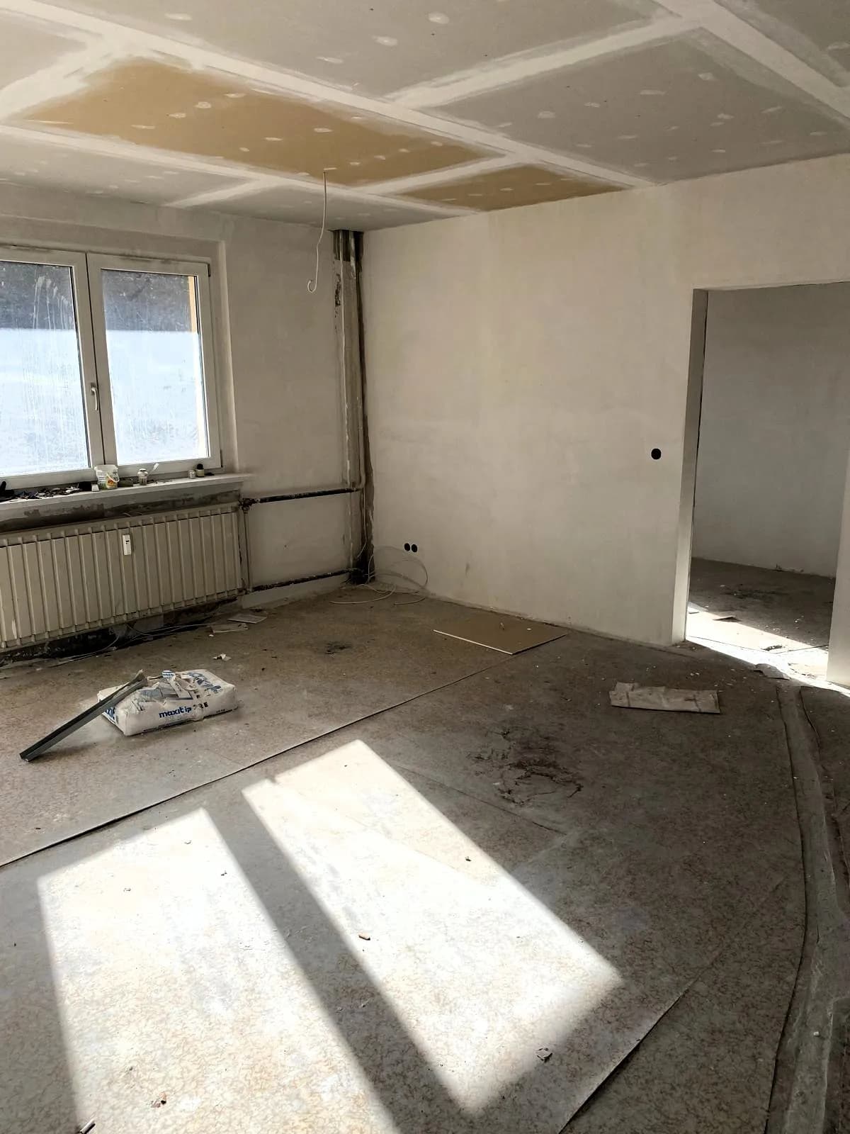 Heller Raum im Zustand der Kernsanierung: verputzte Wände, vorbereitete Trockenbaudecke, Rippenheizkörper und verlegebereiter Estrichboden
