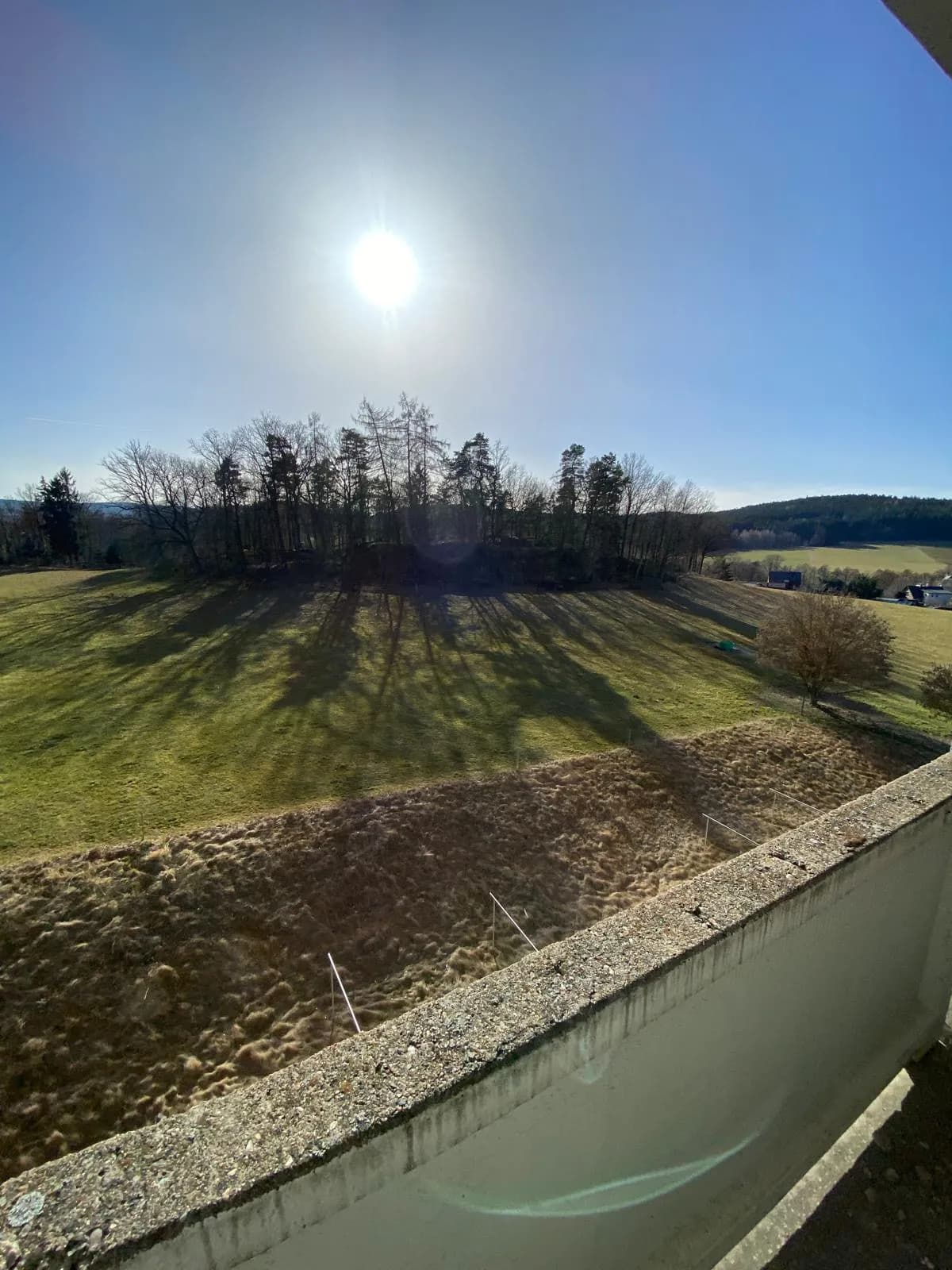Sonniger Weitblick vom Wohnungsbalkon über grüne Wiesen, bewaldete Hügel und die idyllische Naturlandschaft