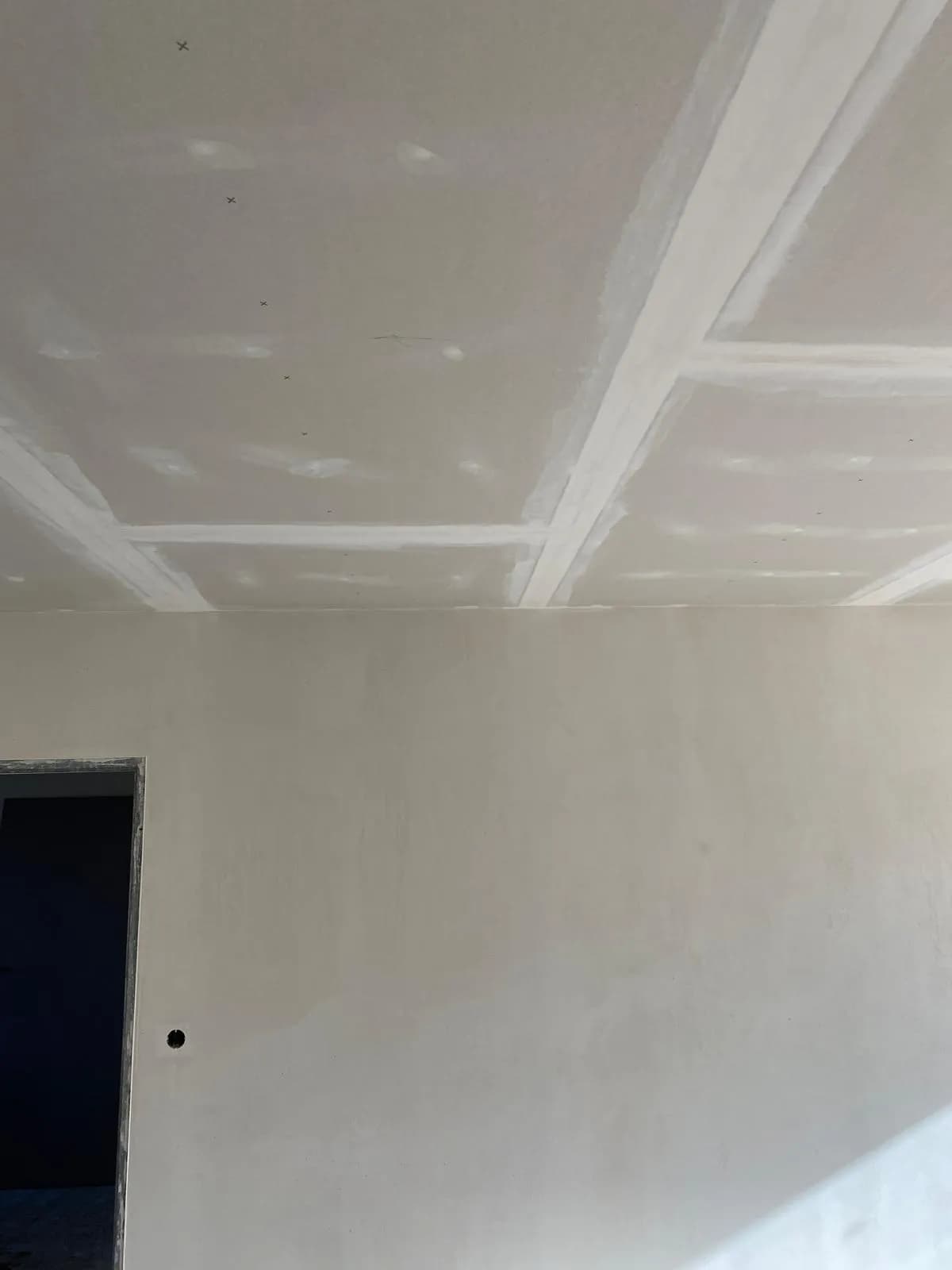 Innenausbau eines Zimmers während der Sanierung: verputzte Wandflächen und abgehängte Trockenbaudecke mit verspachtelten Fugen