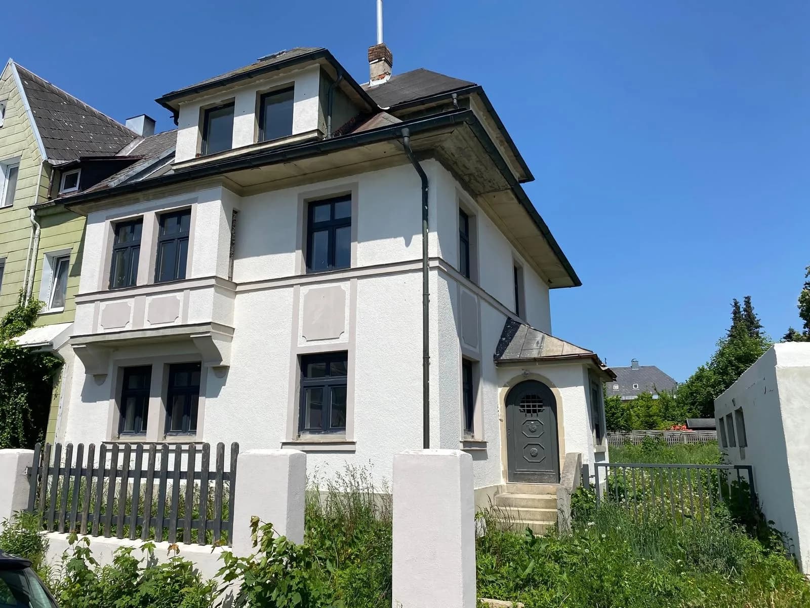 Eckansicht des charmanten Mehrfamilienhauses mit Dachgaube, Erker, überdachtem Eingangsbereich und Holzzaun.