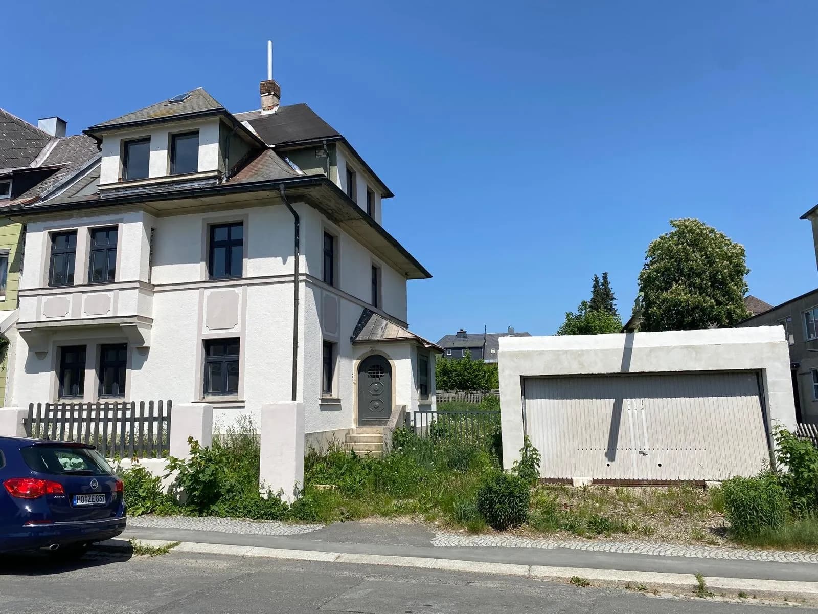 Straßenansicht des freistehenden Mehrfamilienhauses mit weißer Putzfassade, Eingangsbereich, Garage und Parkplatz.