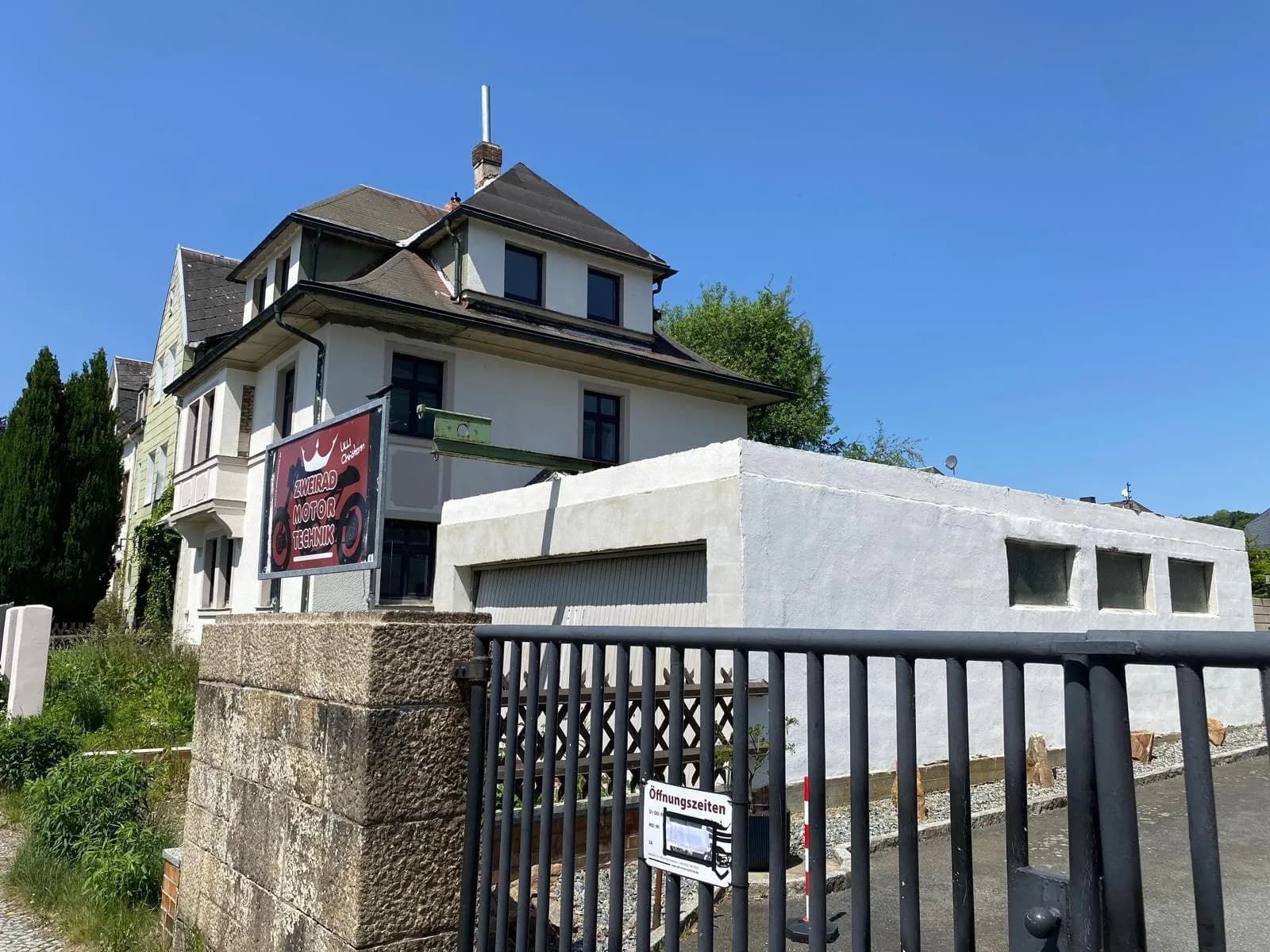 Straßenansicht durch das Hoftor mit Blick auf das Mehrfamilienhaus und das weiße Nebengebäude mit Garage und Werkstatt.