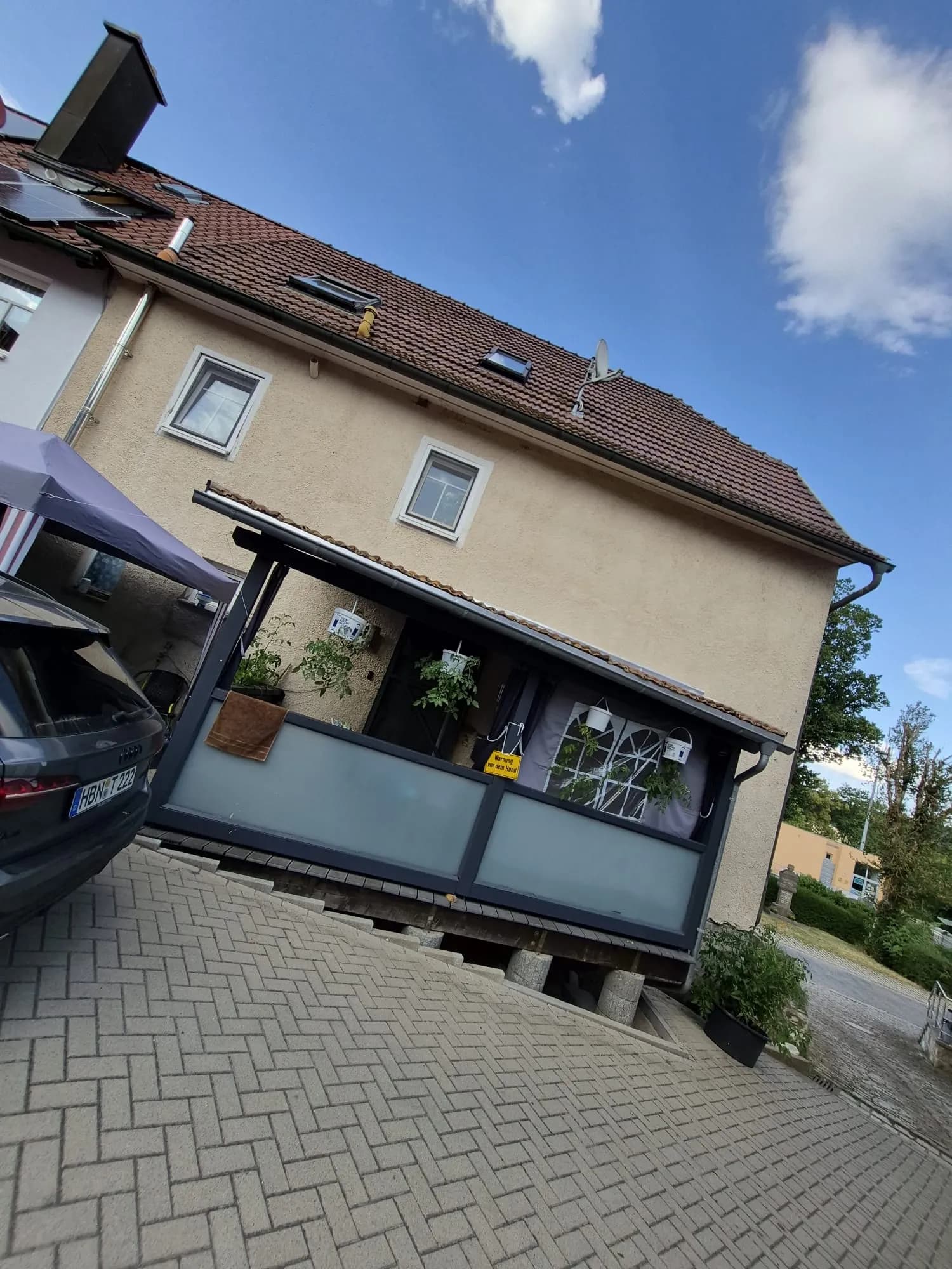 Überdachter, windgeschützter Terrassenbereich mit Sichtschutz-Glaselementen und angrenzendem gepflastertem Hof- bzw. Stellplatzbereich.