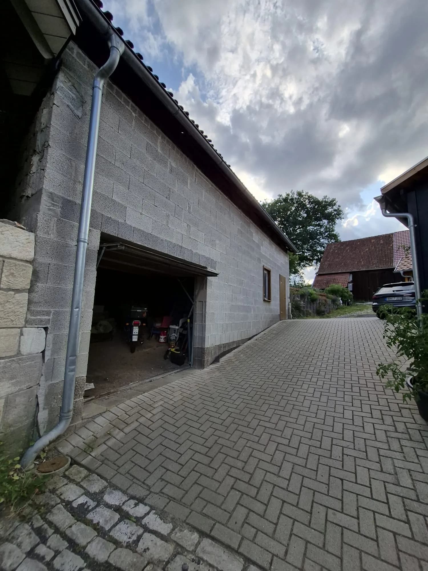 Massives Nebengebäude bzw. Garage mit großem Zufahrtstor, solider Dachentwässerung und gepflasterter Hofzufahrt.