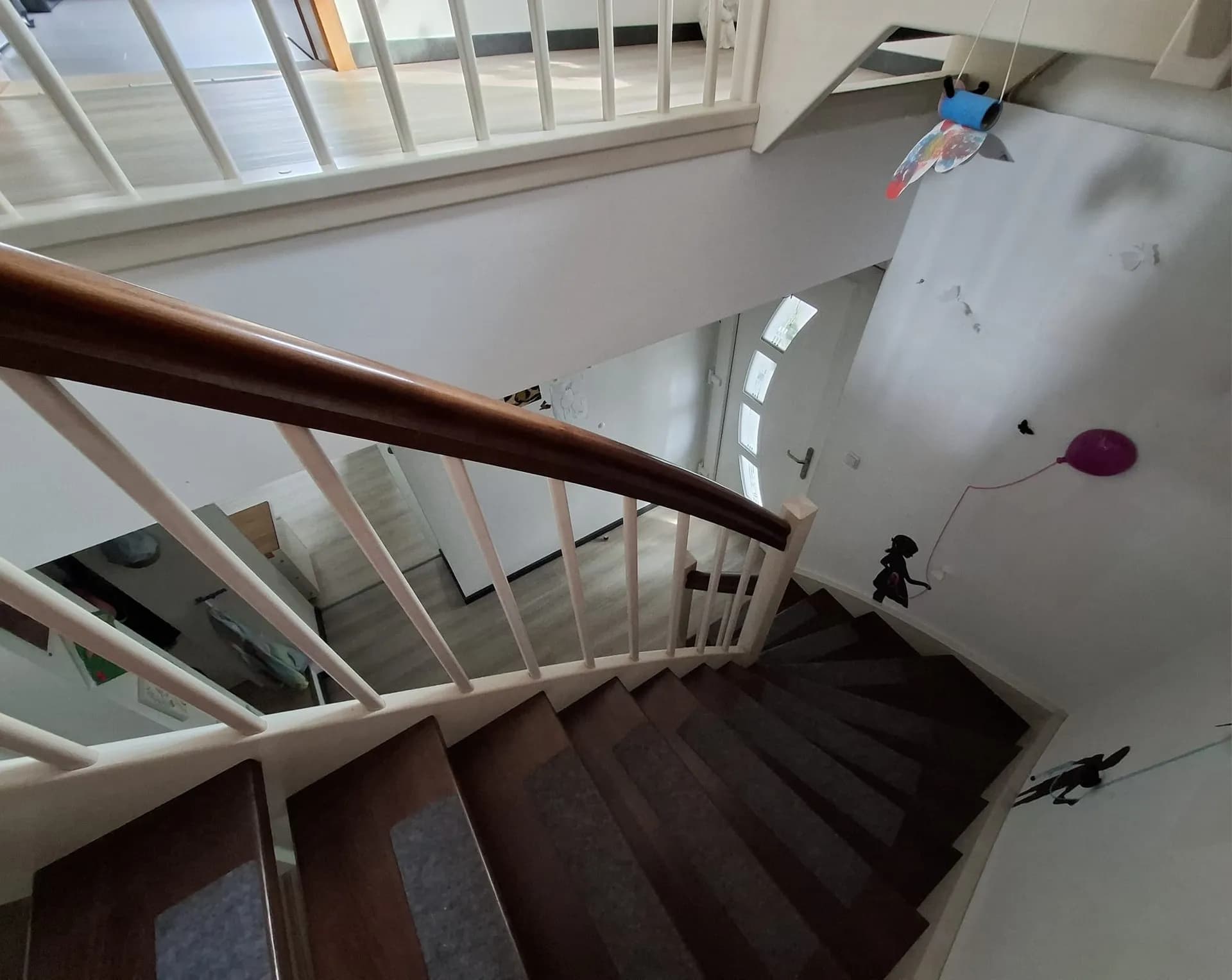 Blick von oben über die geschwungene Holztreppe mit weißem Geländer und dunklen Stufen hinab in den Eingangsbereich.