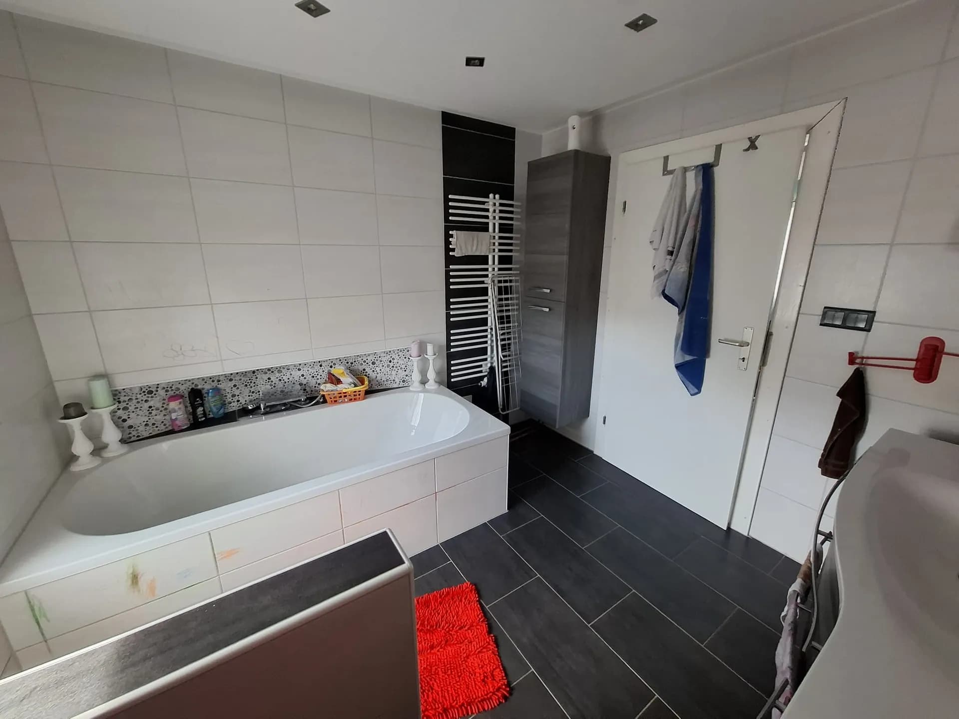 Modernes Badezimmer mit dunklen Bodenfliesen, Einbaubadewanne, Handtuchheizkörper und stilvollem Hochschrank.