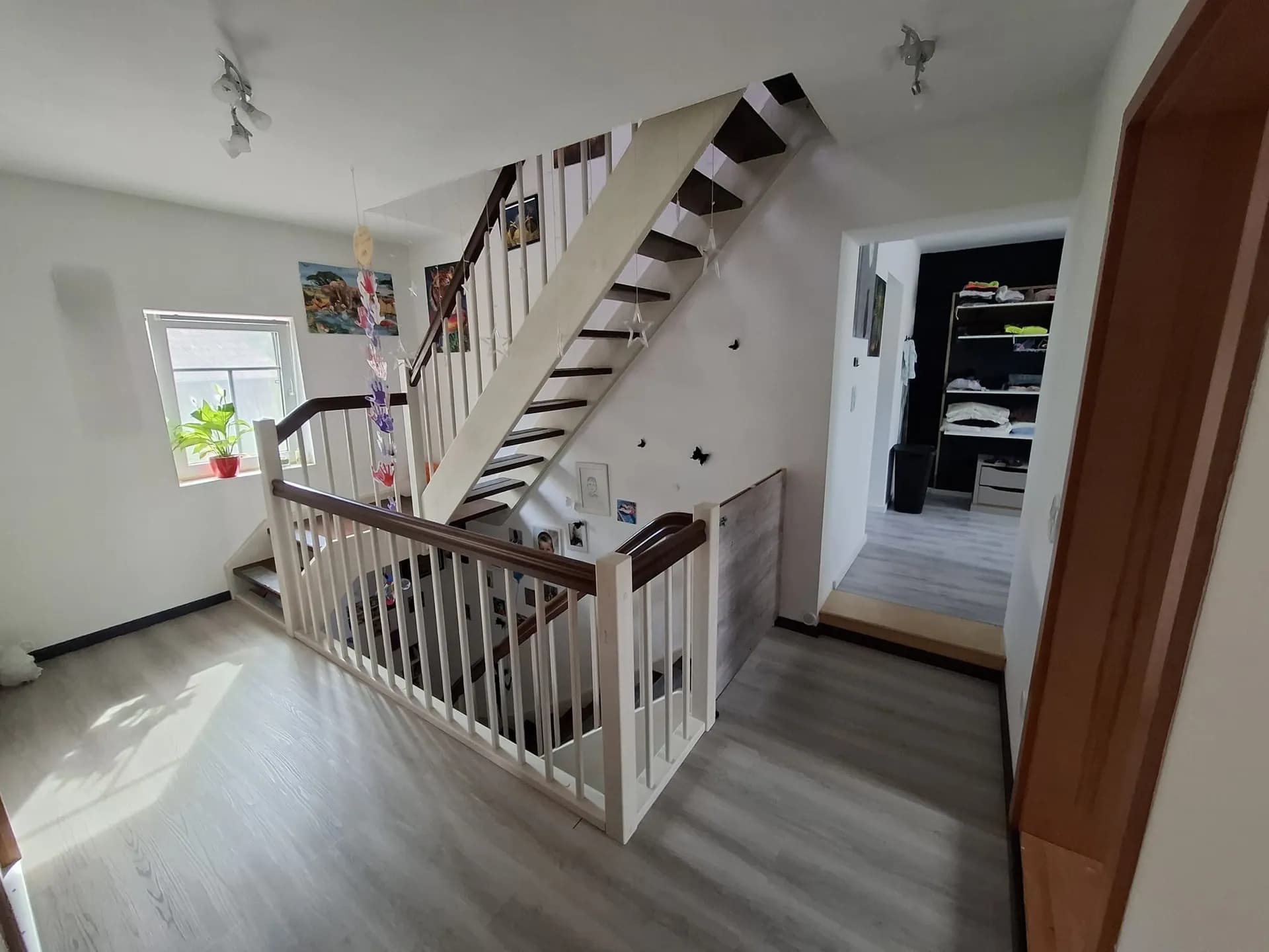 Großzügige Diele im Obergeschoss mit offener Holztreppe, hellem Laminatboden und Zugang zu weiteren Zimmern sowie zum Ankleidebereich.