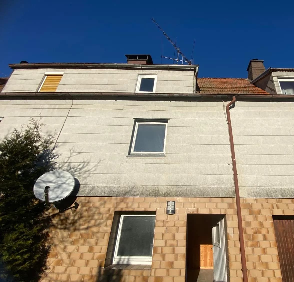 Rückwärtige Fassadenansicht mit Klinkeroptik im Sockelbereich, separatem Hauseingang, Satellitenanlage und Gaubenfenstern.