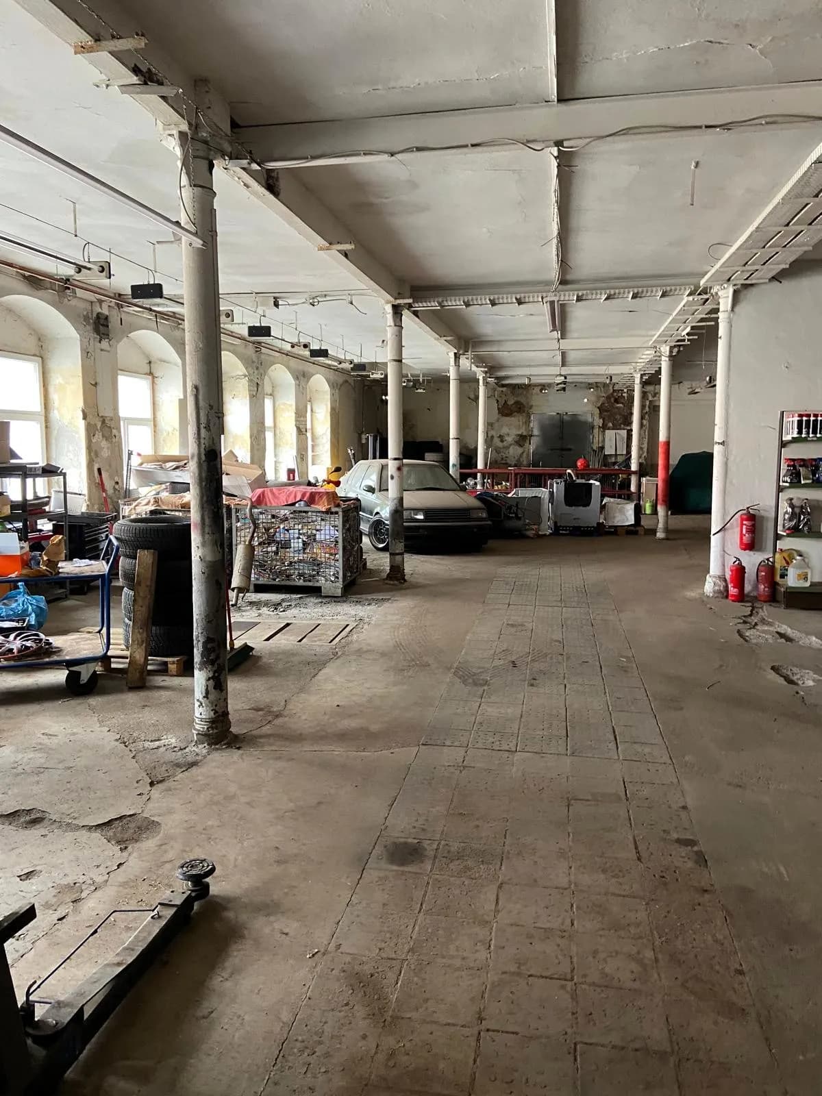 Große Industrie- und Werkstatthalle mit historischen Gusseisensäulen, Bogenfenstern, Werkstattbereich und befahrbarem Industrieboden.