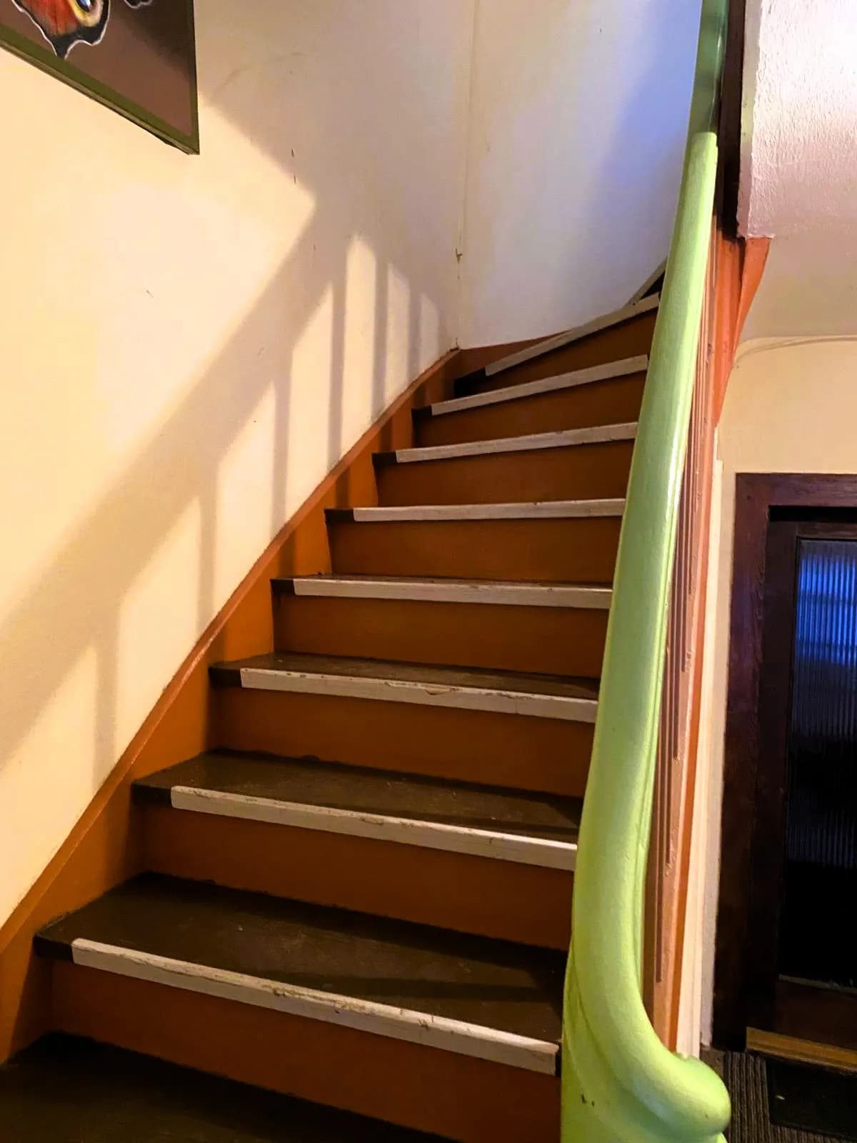 Klassisches Treppenhaus mit massiver Holztreppe, Handlauf und Trittkantenschutz auf den Stufen.