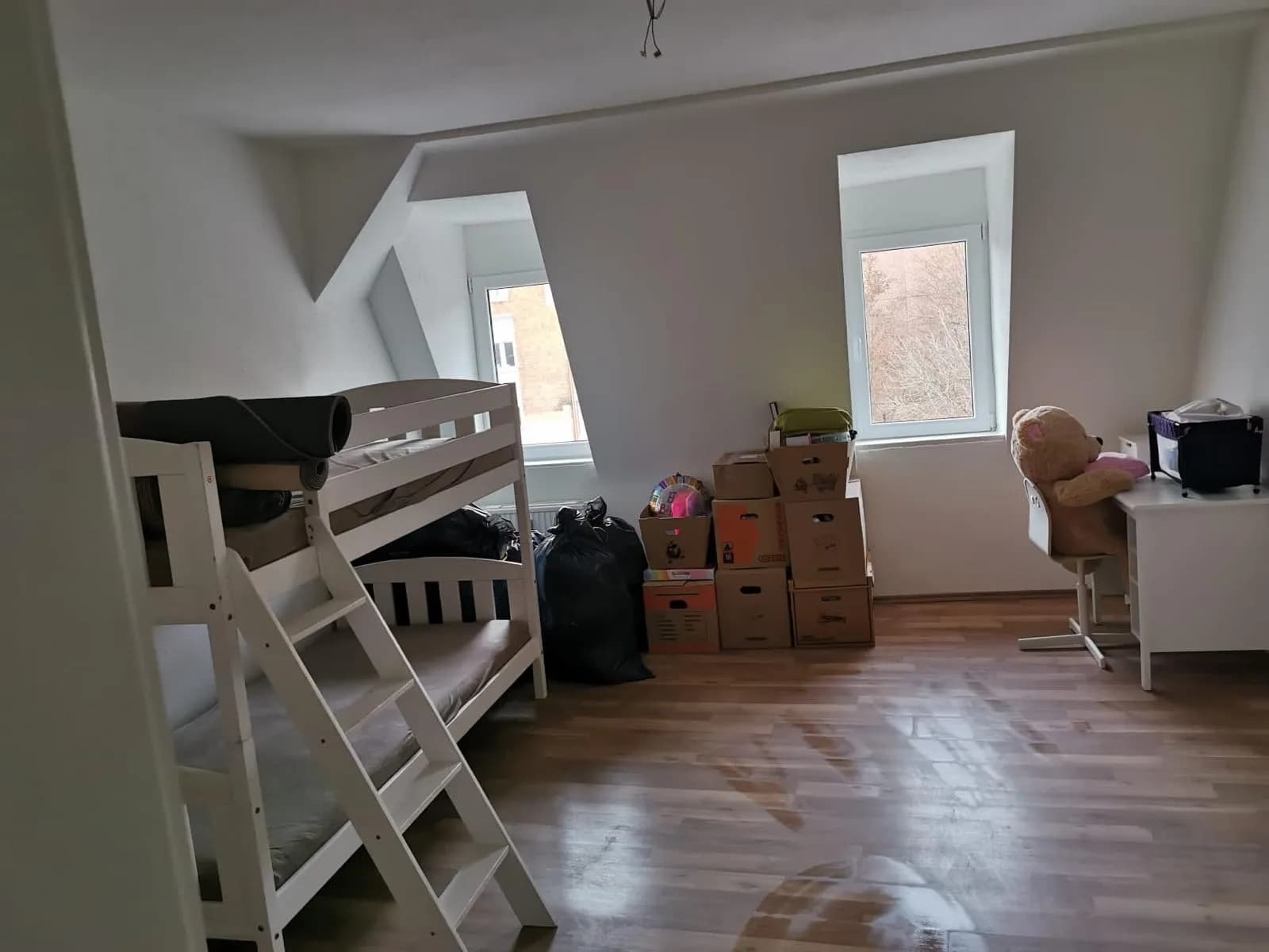 Helles Dachgeschosszimmer mit Holzoptik-Laminatboden, zwei Gaubenfenstern, Etagenbett und Arbeitsbereich mit Schreibtisch.