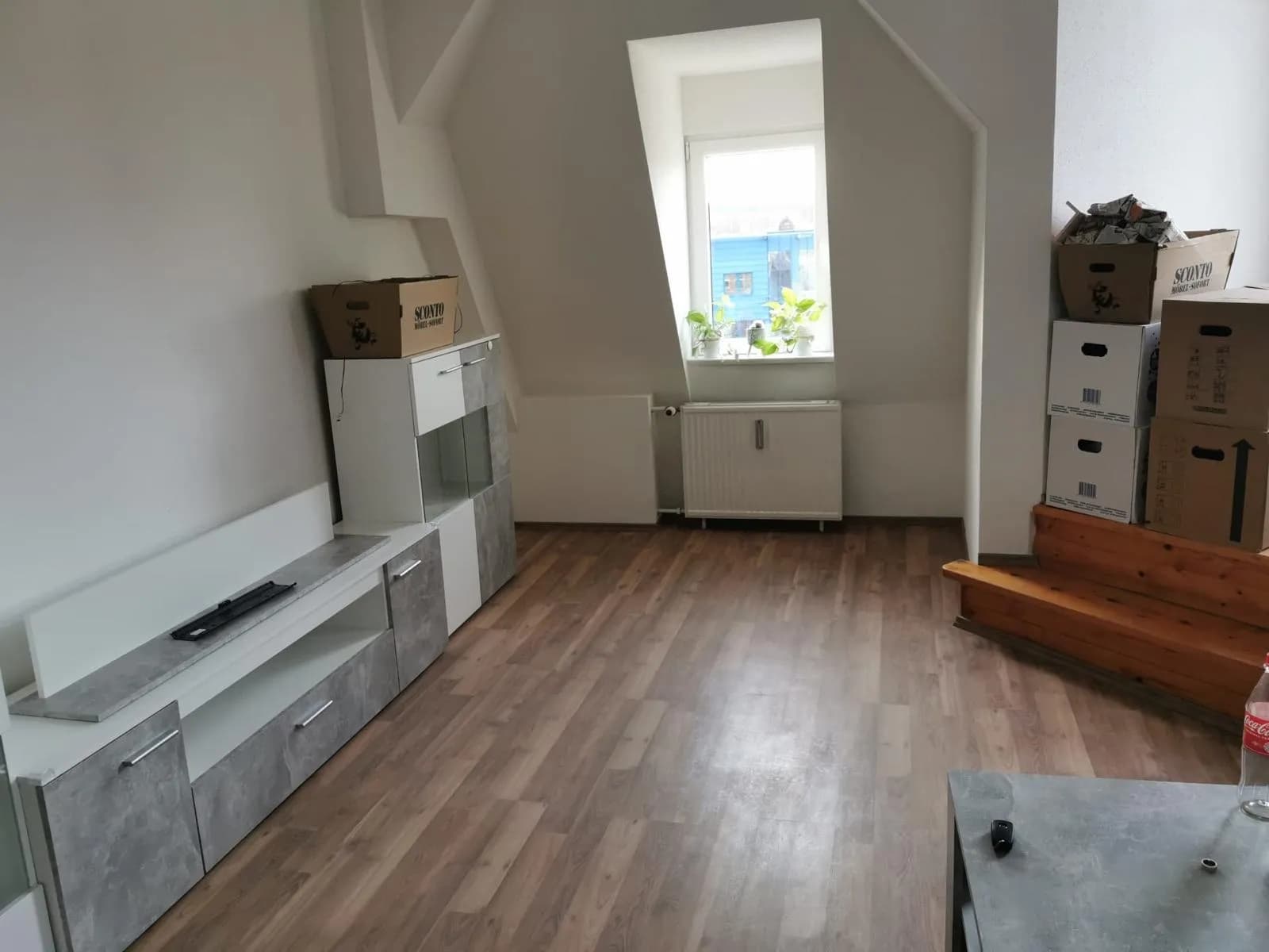 Geräumiger Wohnbereich im Dachgeschoss mit Dachschrägen, Laminatboden, moderner TV-Wohnwand, Heizkörper und Tageslichtfenster.