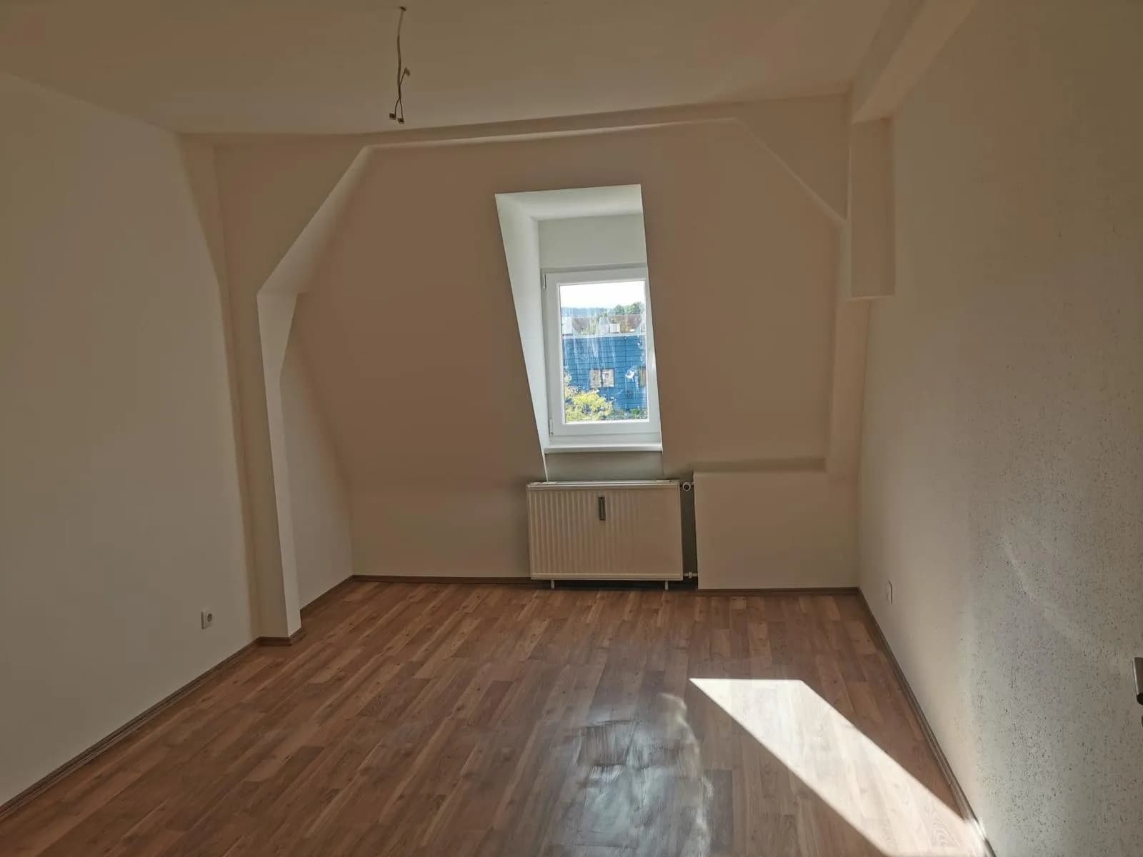 Hell renoviertes Dachgeschosszimmer mit zwei Gaubenfenstern, Heizkörper, frisch gestrichenen Wänden und warmem Laminatboden.