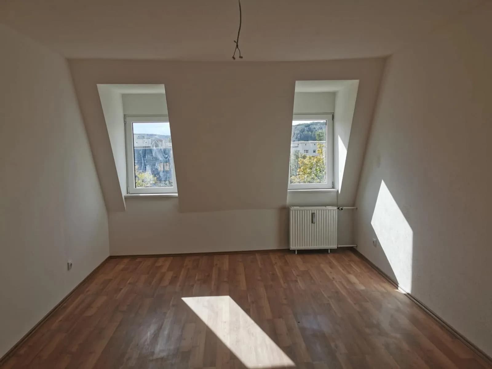 Dachgeschoss-Wohnraum mit Gaubenfenster, Laminatboden, Heizkörper und erhöhter Holzdielen-Podestebene mit Stufen.