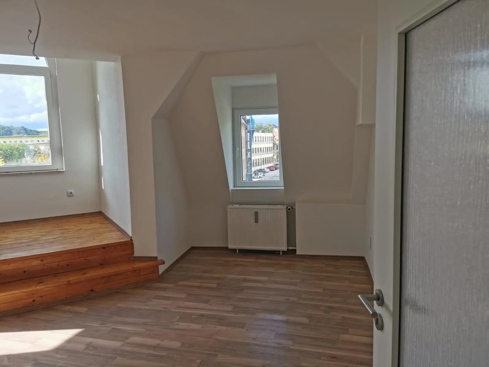 Großzügiges Zimmer im Dachgeschoss mit charakteristischen Dachschrägen und Nischen, Gaubenfenster, Heizkörper und gepflegtem Laminatbelag.