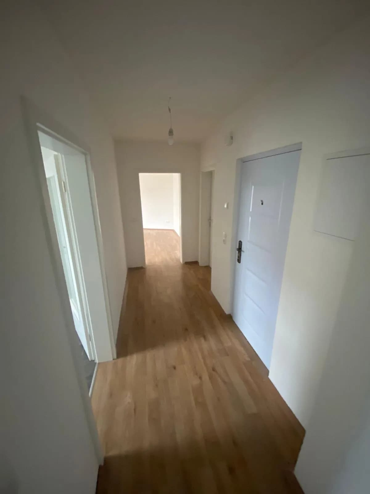 Eingangsbereich und Flur der Wohnung mit warmem Holzlaminat, frisch geweißten Wänden und weißen Zimmertüren zu allen Räumen.