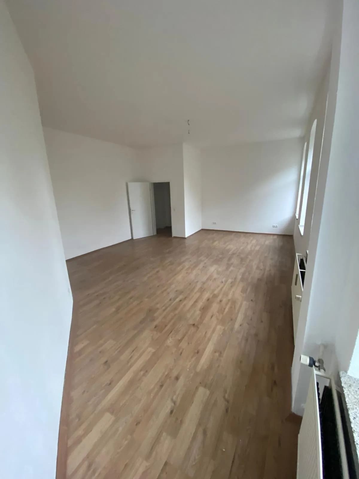 Sehr großzügiger und heller Wohnraum mit warmem Laminatboden, frisch geweißten Wänden, Heizkörper und hohen Fenstern.