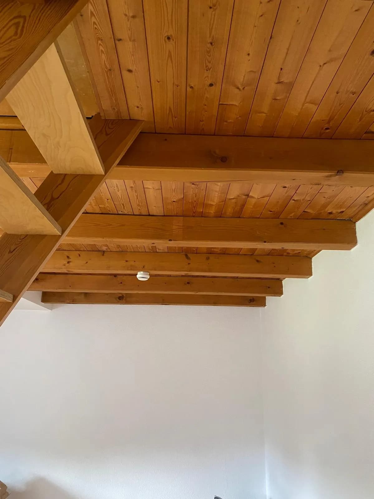 achgeschoss-Detailansicht mit massiver Holzbalkendecke, Sichtschalung, Rauchmelder und Zugangstreppe zur offenen Galerie.