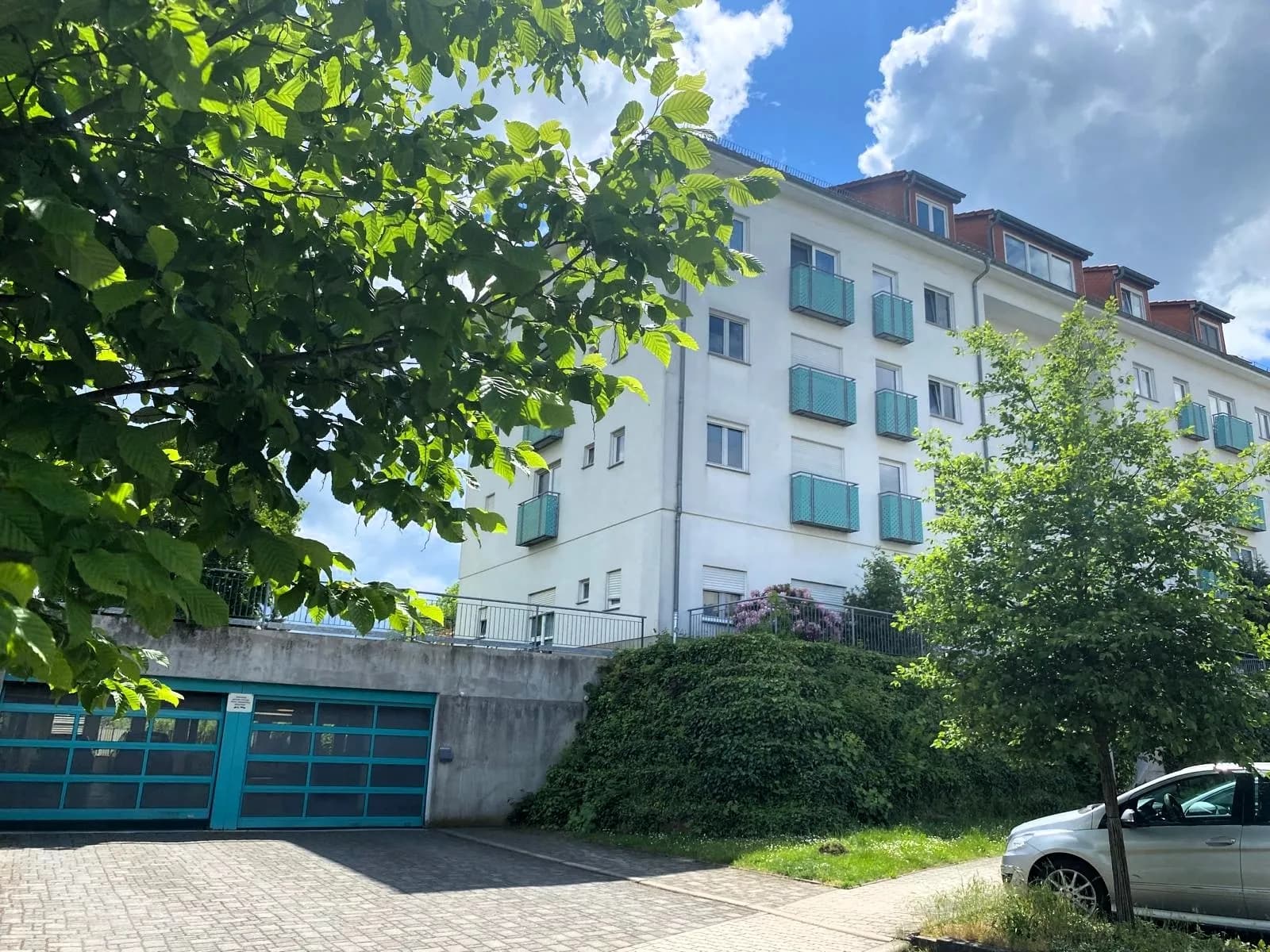 Perspektivische Ansicht des Wohnkomplexes mit gepflasterter Zufahrt, Tiefgarageneinfahrt und gepflegten Grünanlagen.