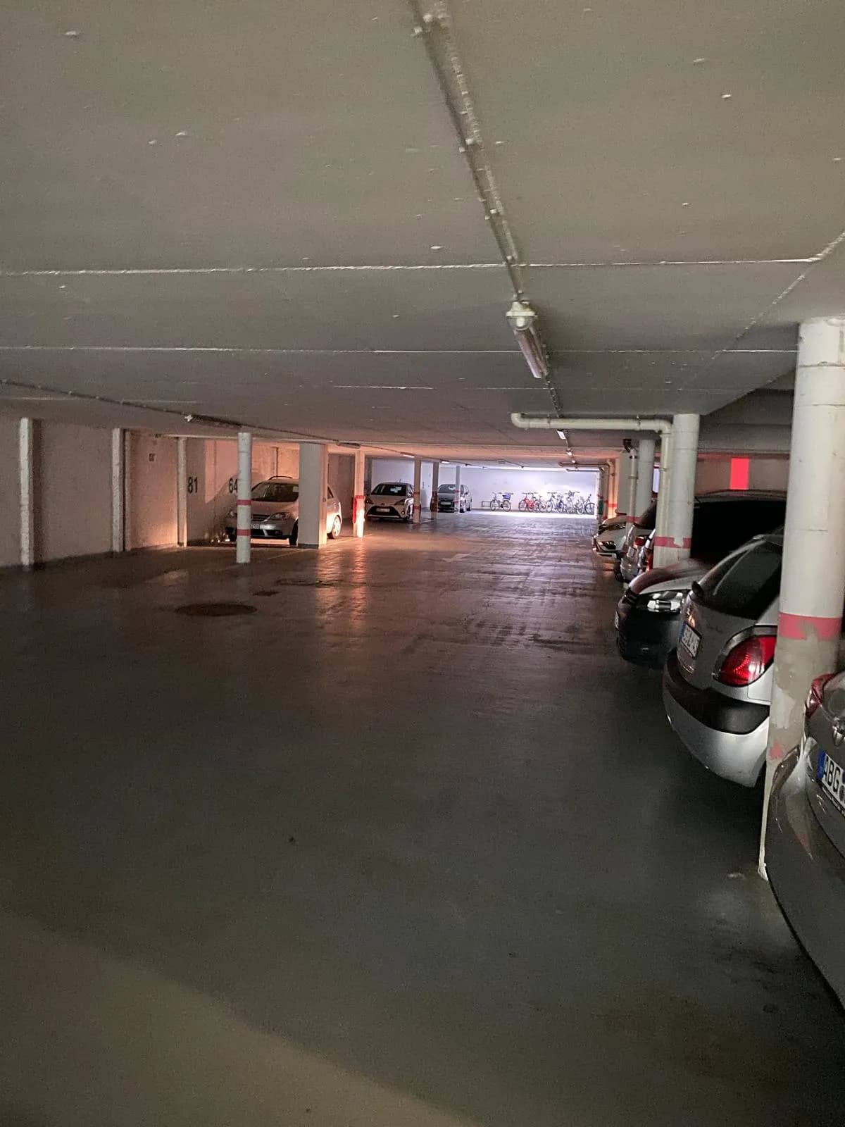 Großzügige Tiefgarage mit markierten Pkw-Stellplätzen, Betonpfeilern, Deckenbeleuchtung und Fahrradabstellbereich im Hintergrund.