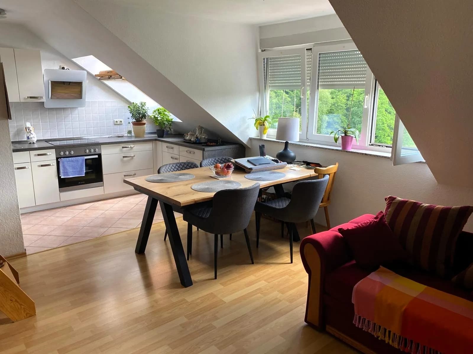 Gemütliche Dachgeschoss-Wohnküche mit Essbereich, Dachflächenfenster, Einbauküche, Sofa und schönem Weitblick ins Grüne.