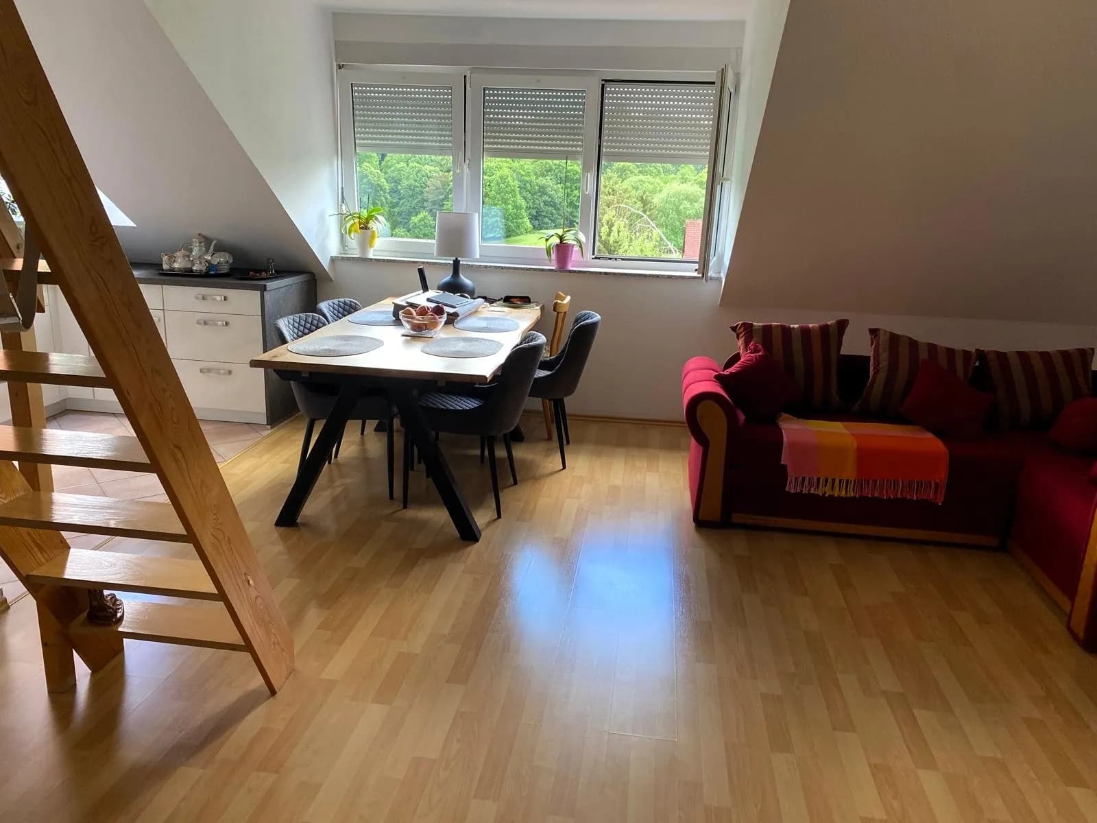 Offener, lichtdurchfluteter Dachgeschoss-Wohnbereich mit Laminatboden, Essgruppe, gemütlichem Sofa, offener Holztreppe zur Galerie und herrlichem Grünblick.