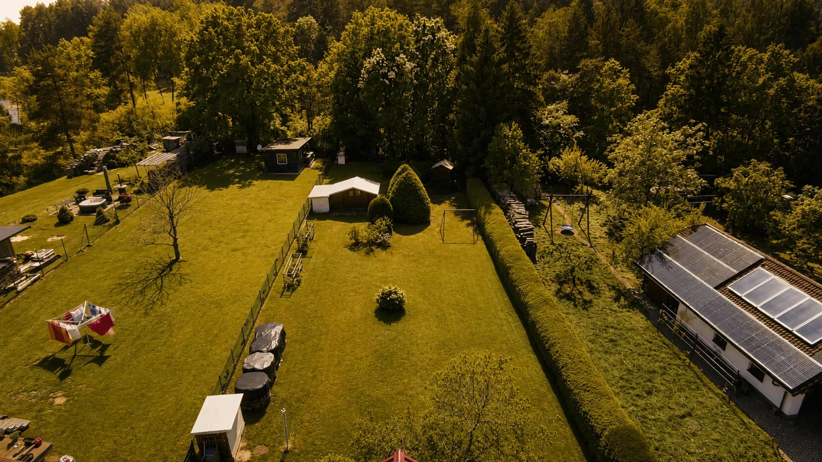 Luftaufnahme des Einfamilienhauses mit großem Gartengrundstück, eingezäunter Rasenfläche und Blick ins Grüne.